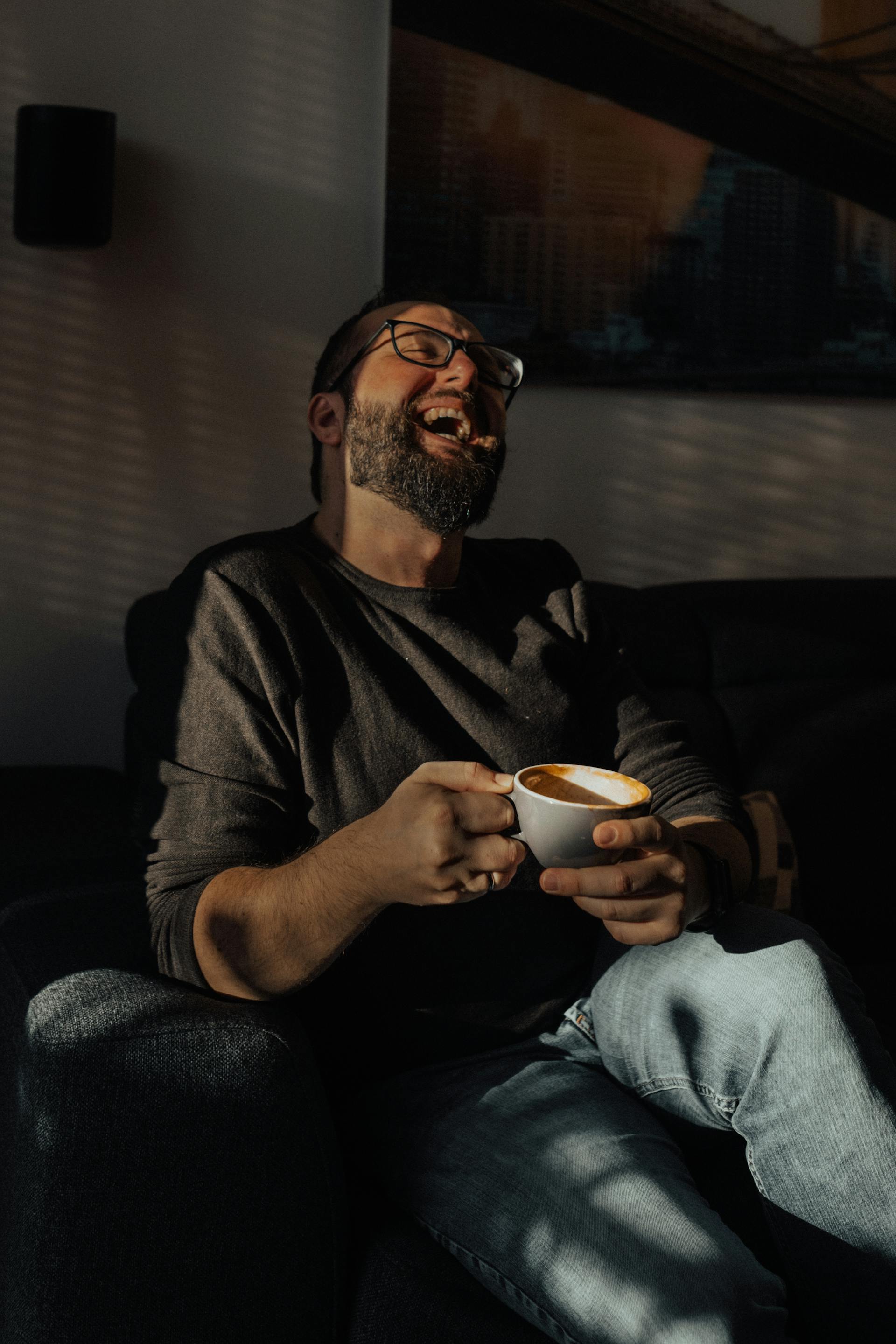 Un hombre riendo mientras sostiene una taza de café | Fuente: Pexels