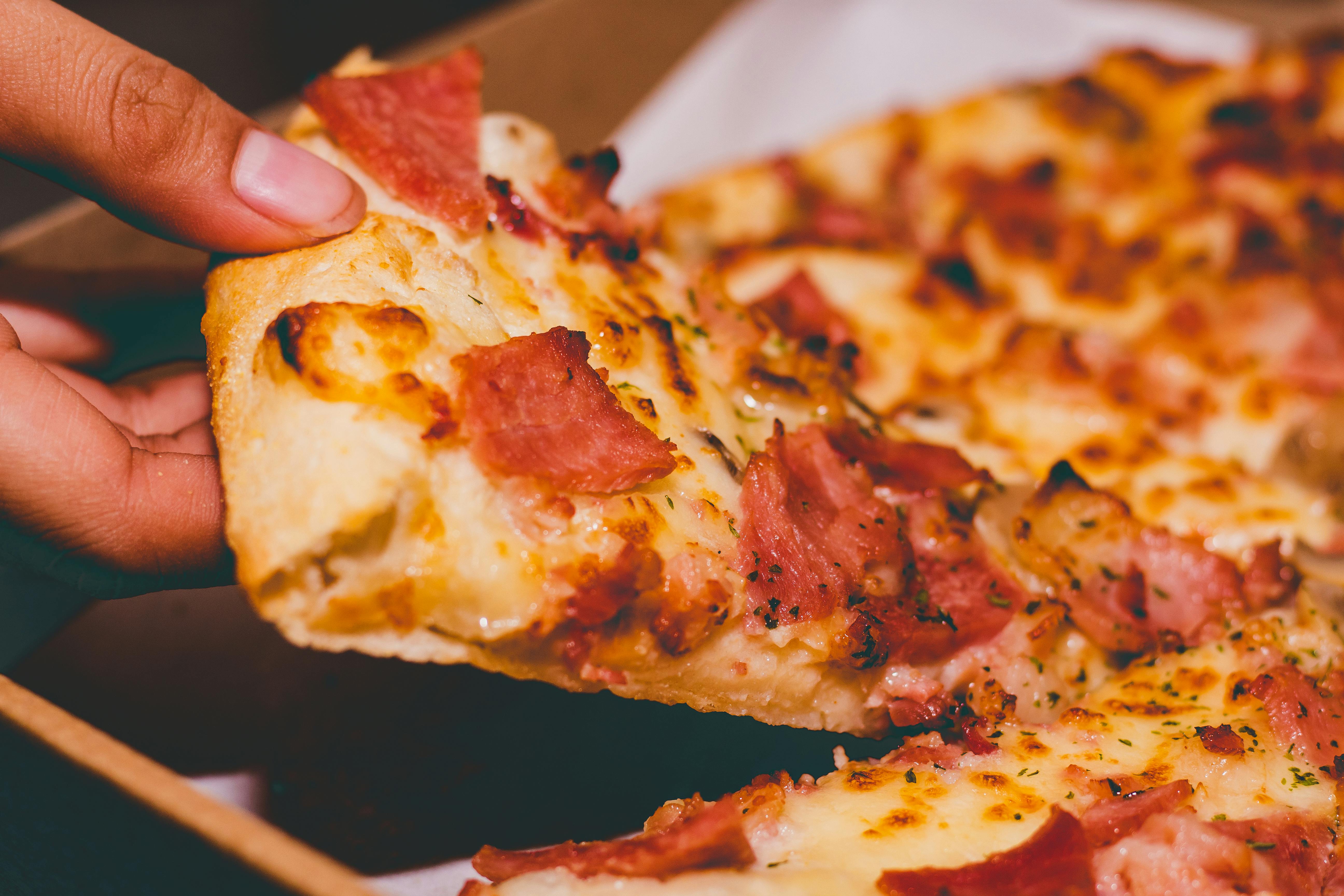 Una persona sujetando una porción de pizza | Fuente: Pexels