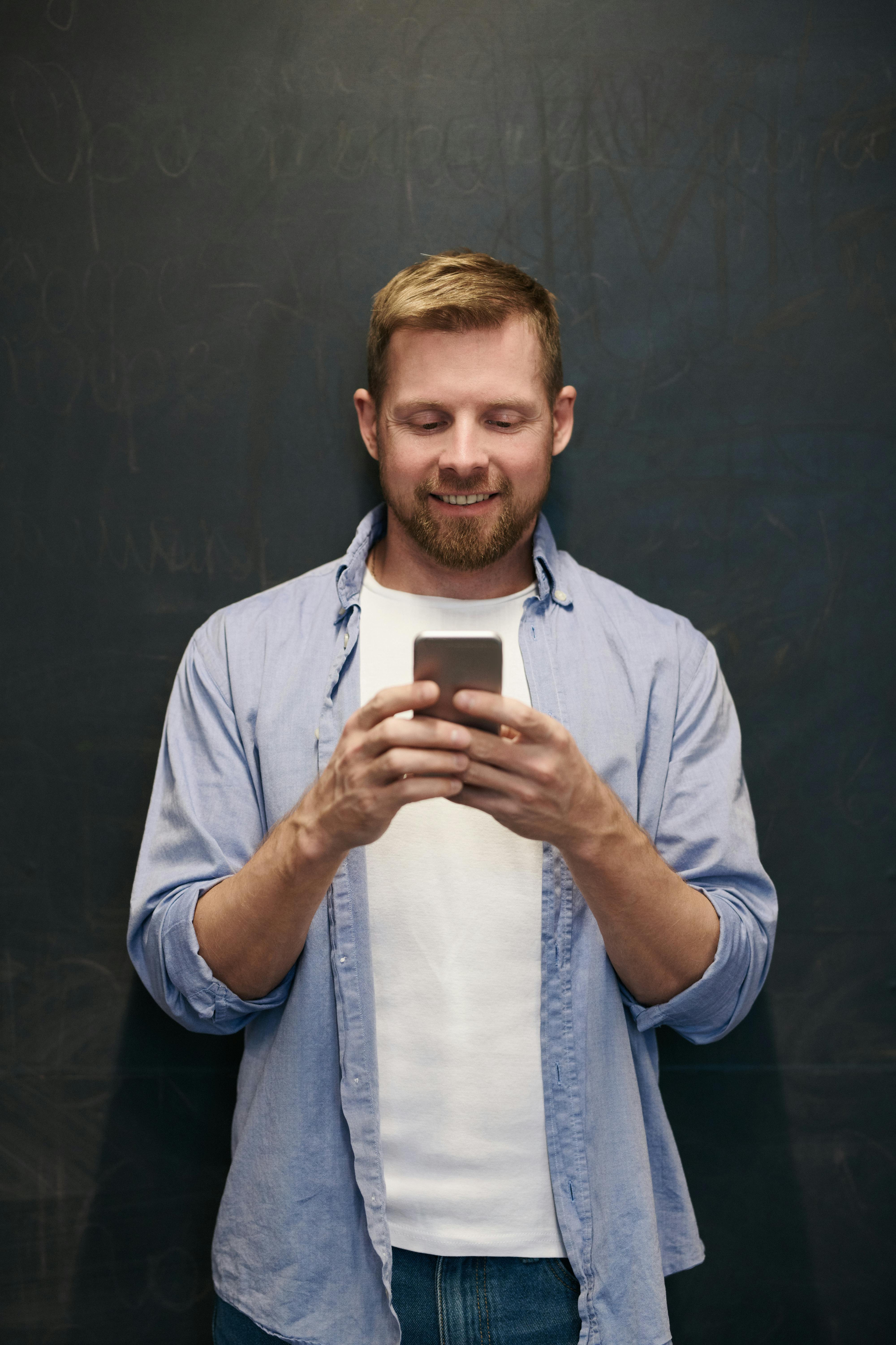 Un hombre sonriente cogiendo su teléfono | Fuente: Pexels