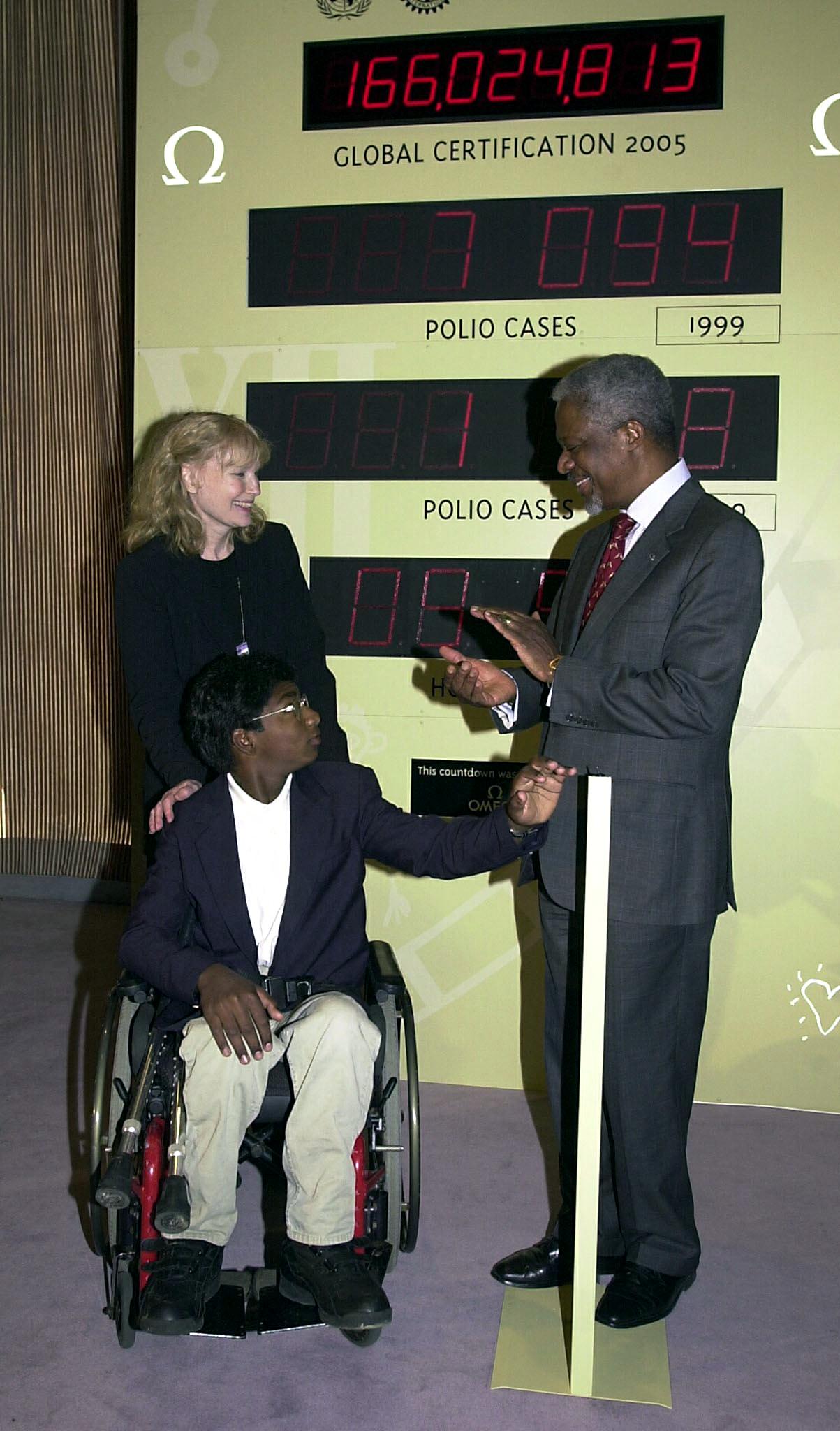 Kofi Annan (dcha.) aplaude mientras Thaddeus Farrow (cda.), hijo adoptivo de Mia Farrow (izda.), acciona el interruptor para poner en marcha un reloj que iniciará la cuenta atrás hacia un mundo libre de polio en 2005, el 27 de septiembre de 2000. | Fuente: Getty Images