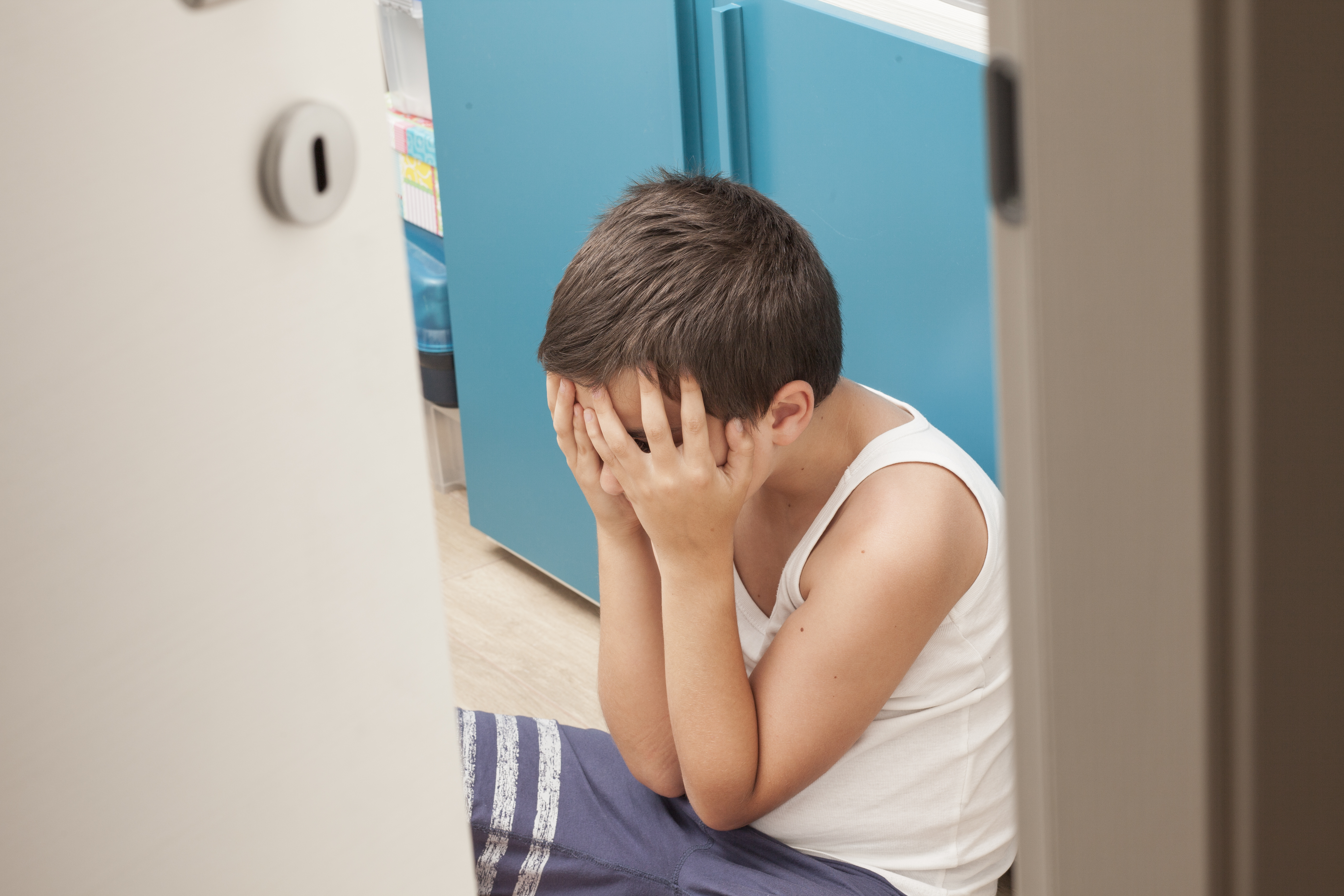 Niño cubriéndose la cara con las manos sentado en el suelo. | Foto: Shutterstock