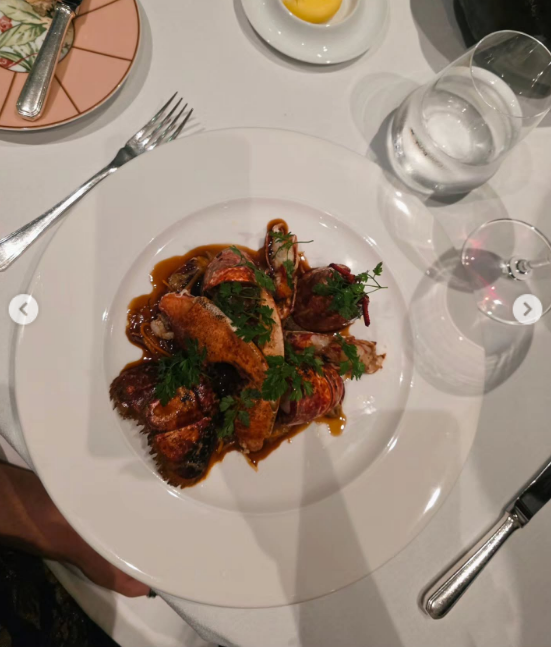 La modelo compartió una cuidada postal culinaria de un plato gourmet servido sobre vajilla blanca en un restaurante elegante. La preparación presenta piezas de mariscos glaseados en una salsa oscura y aromática, decorados minuciosamente con hierbas frescas en una mesa dispuesta con copas de cristal y cubiertos finos. | Fuente: Instagram/emilia_att