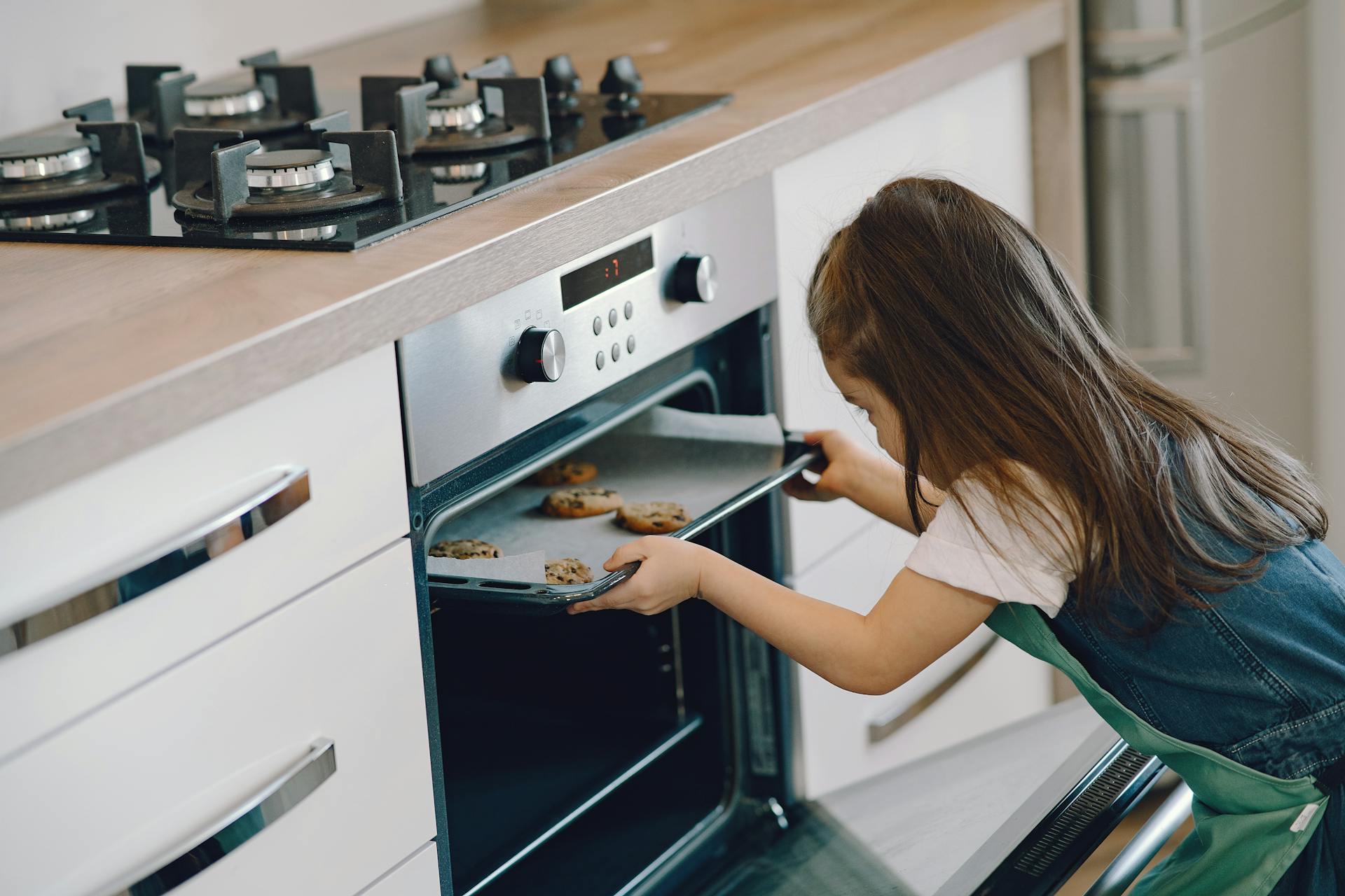 Una chica metiendo una bandeja de galletas en el horno | Fuente: Pexels