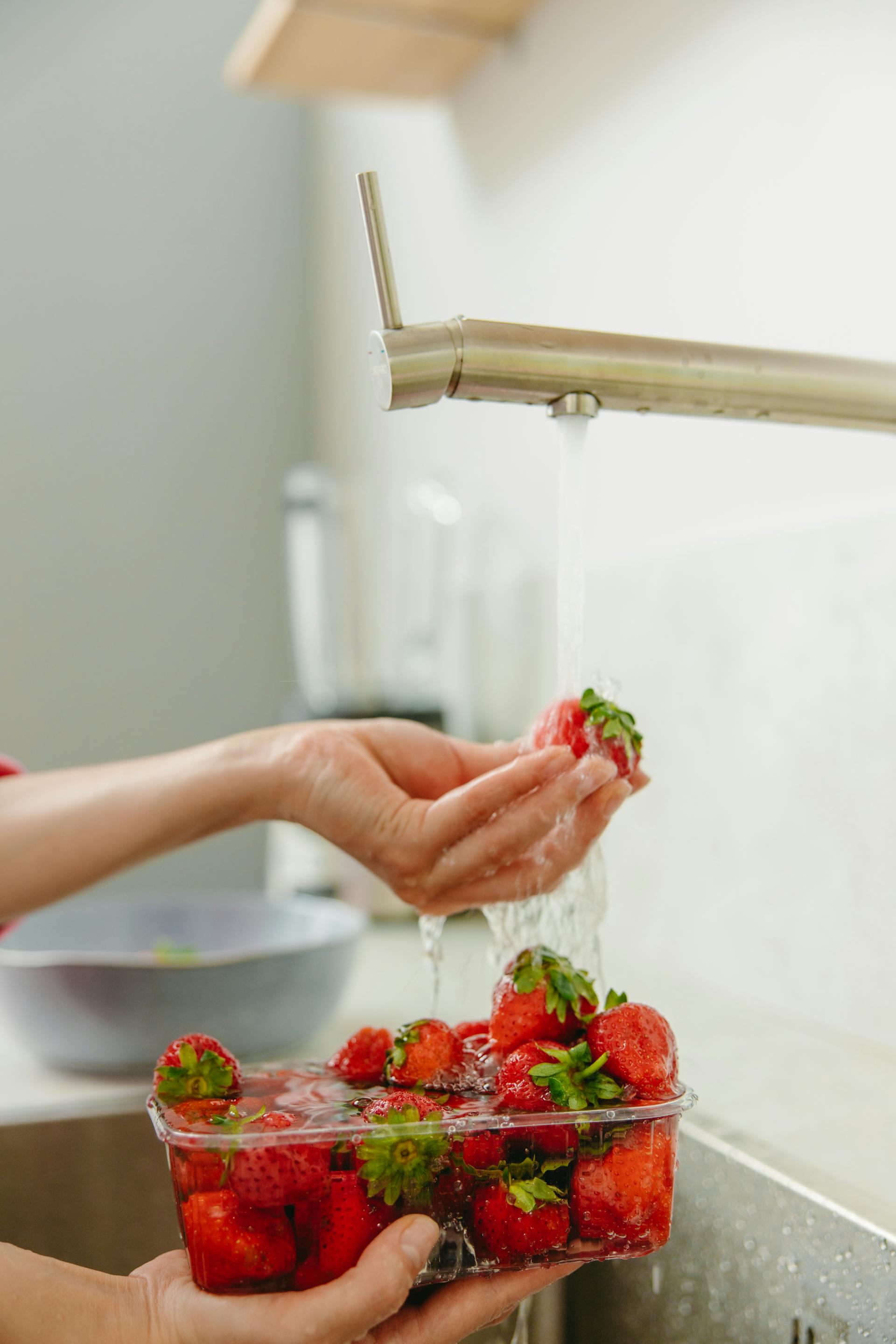 Primer plano de una mujer lavando fresas con agua corriente en la cocina | Fuente: Pexels