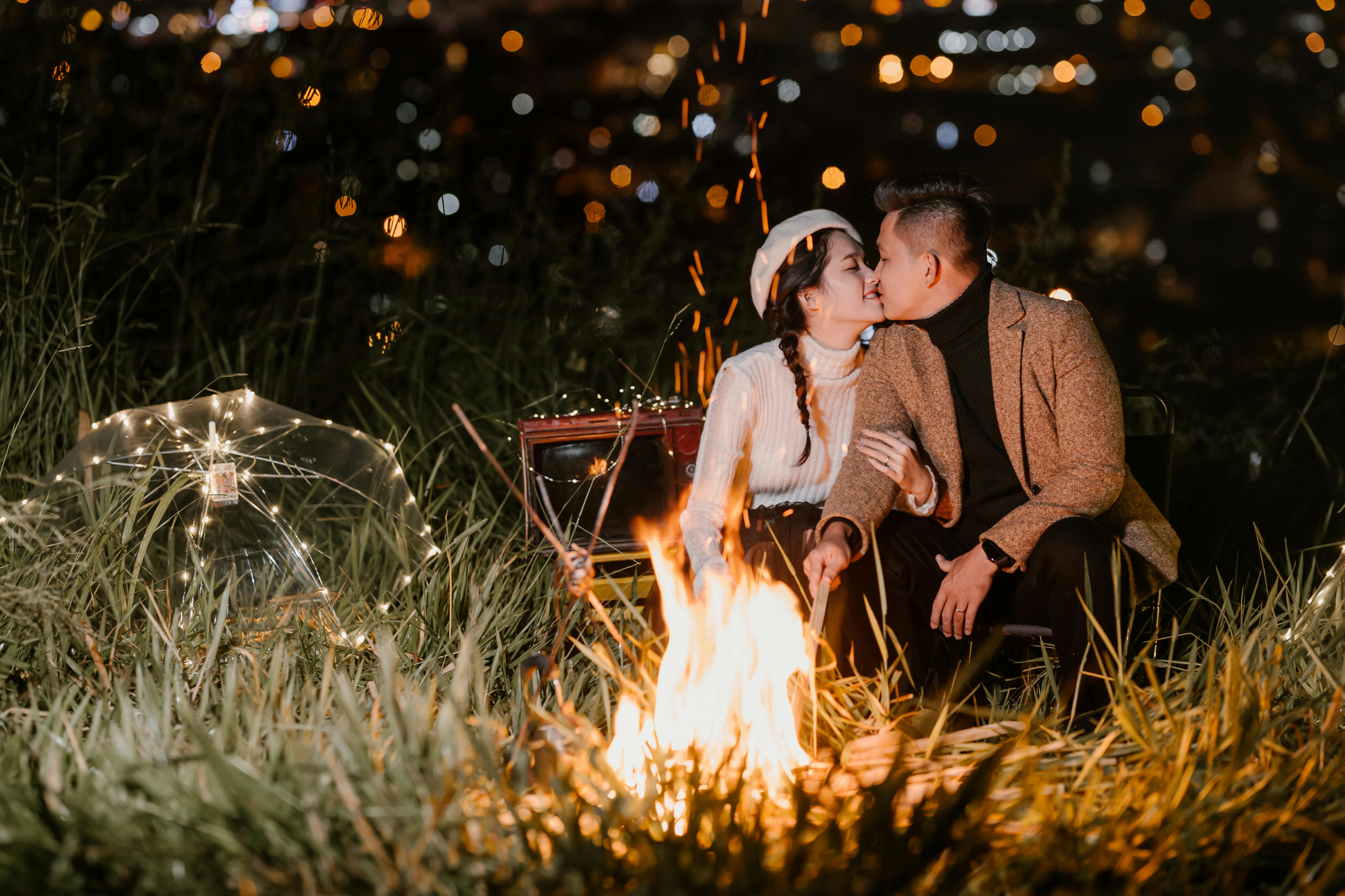 Una pareja besándose bajo la luz de la luna con una hoguera encendida | Fuente: Pexels