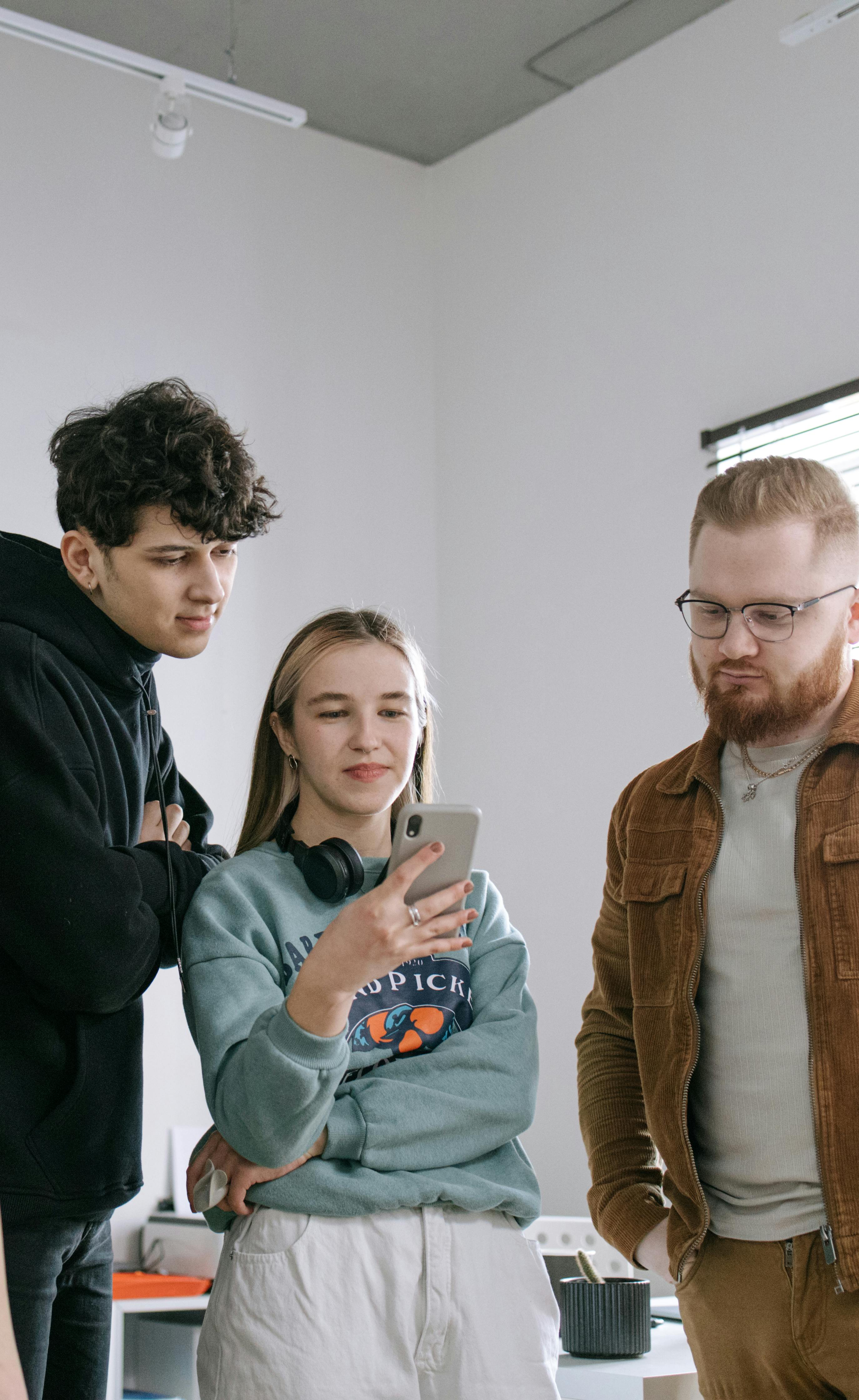 Una mujer y dos hombres mirando un teléfono mientras traman algo | Fuente: Pexels