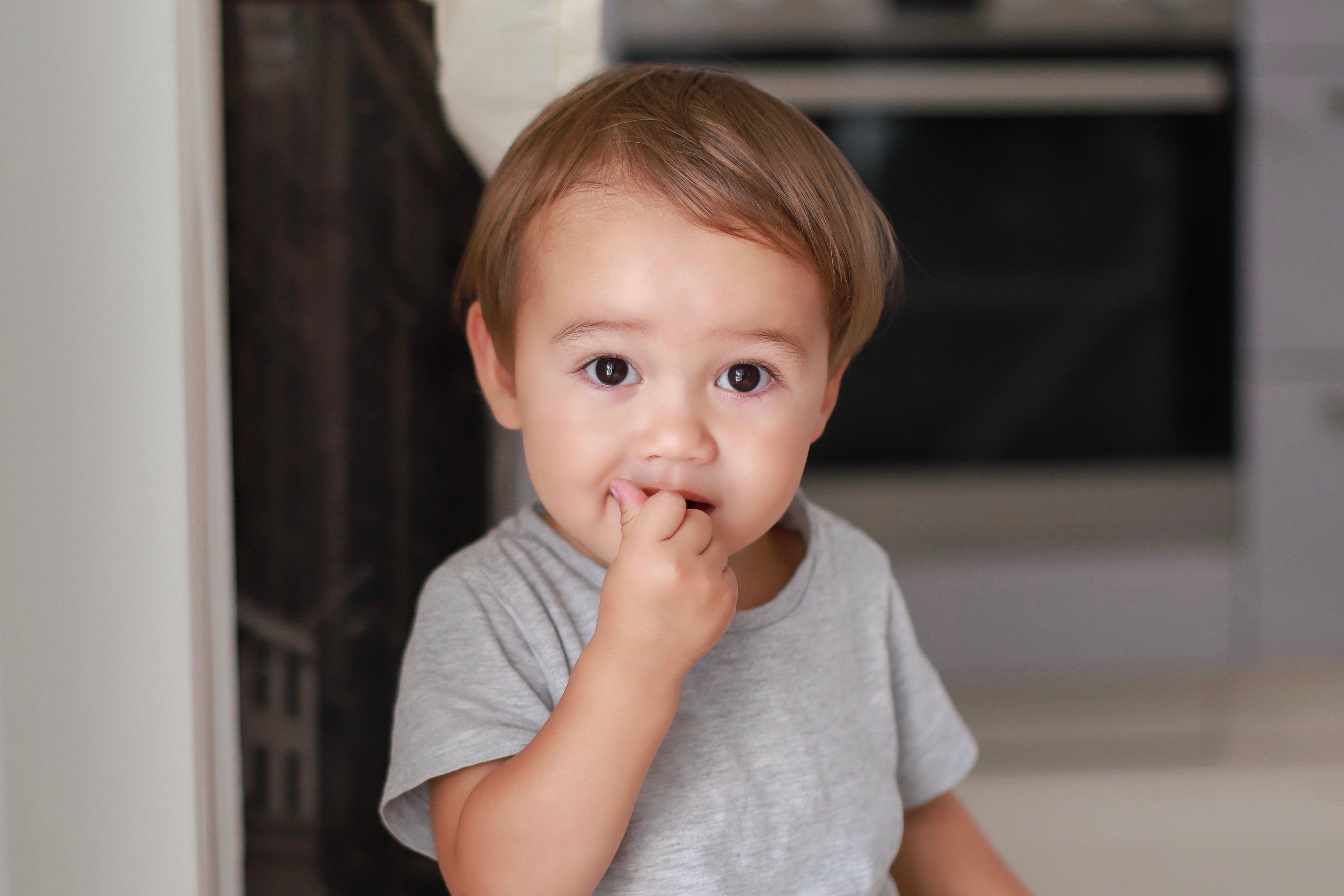 Retrato de cabeza de un simpático bebé con el dedo dentro de la boca comiendo un bocadillo en casa. | Fuente: Shutterstock