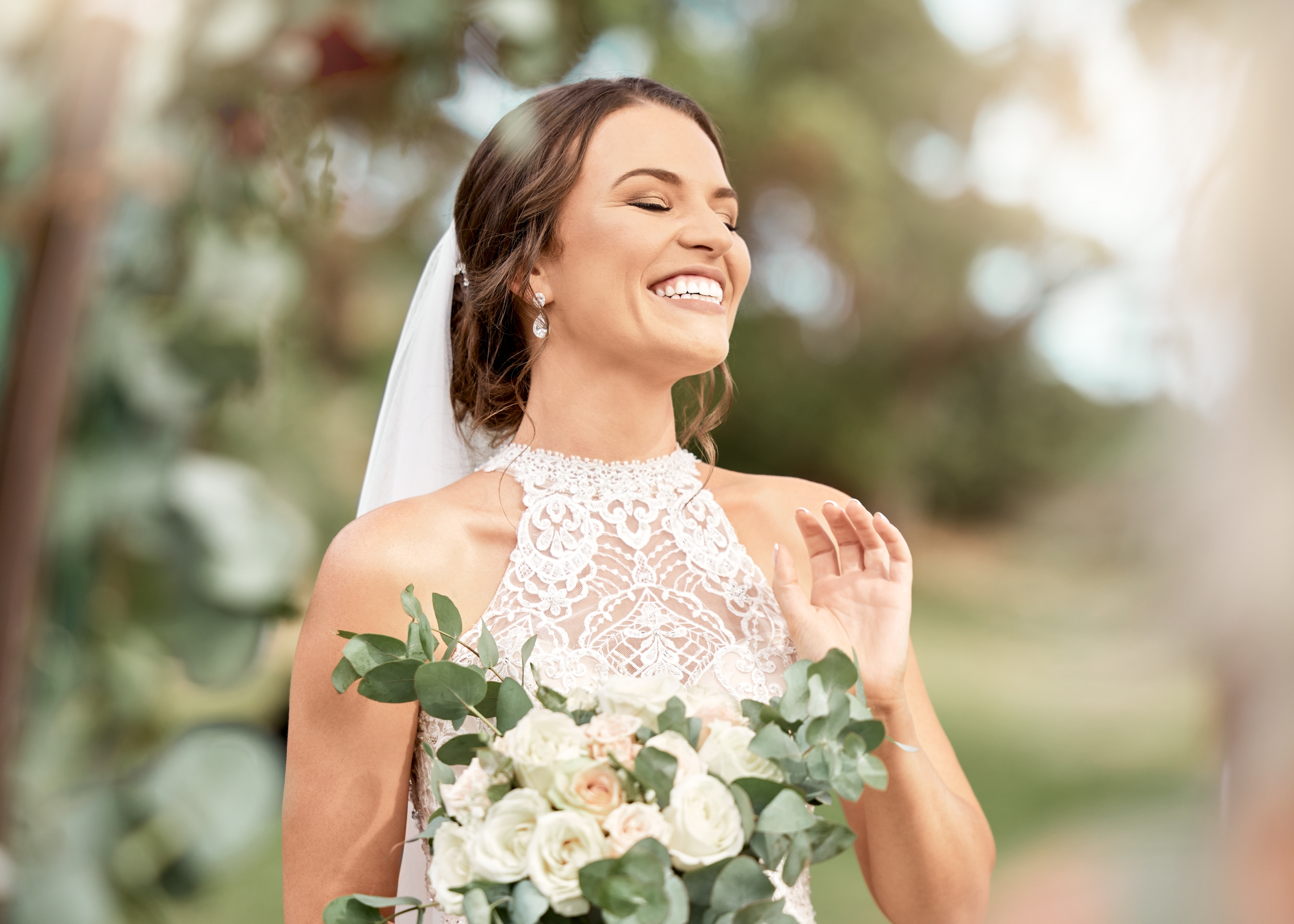 Novia emocionada en boda con ramo en parque natural con árboles verdes, bokeh y sol de verano. Felicidad, compromiso y sueño de una mujer bella con flores para casarse en un destello de lente al aire libre | Fuente: Getty Images