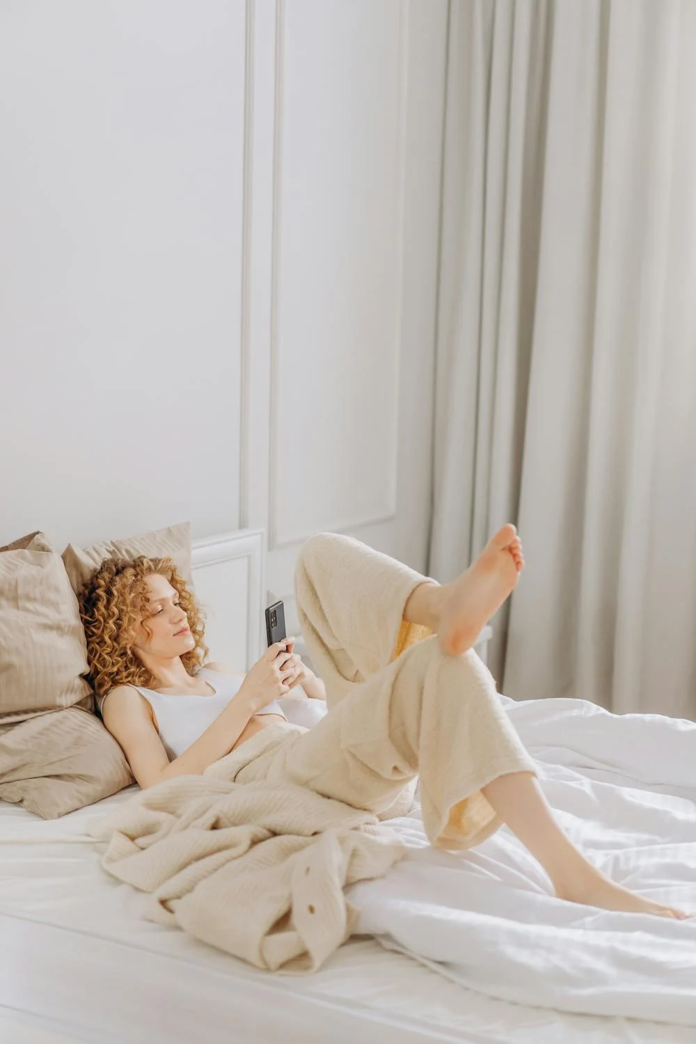 Una mujer feliz hablando por teléfono en su cama ⏐ Fuente: Pexels