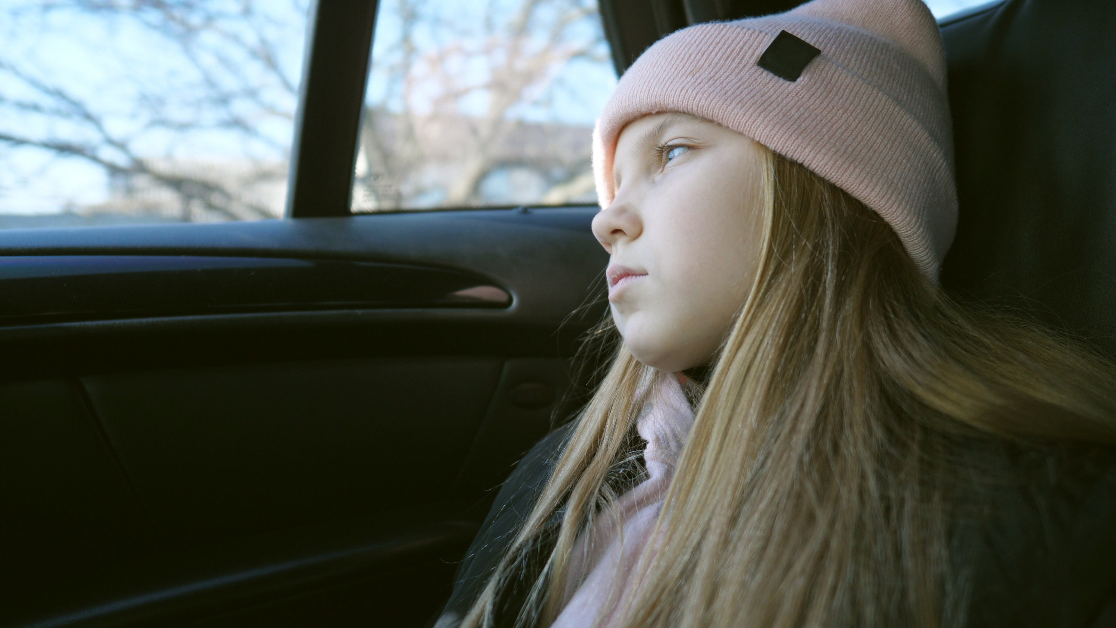 Hermosa chica de pelo largo y rubio mira al exterior a través de la ventanilla en el asiento trasero de un Automóvil en marcha | Fuente: Shutterstock.com