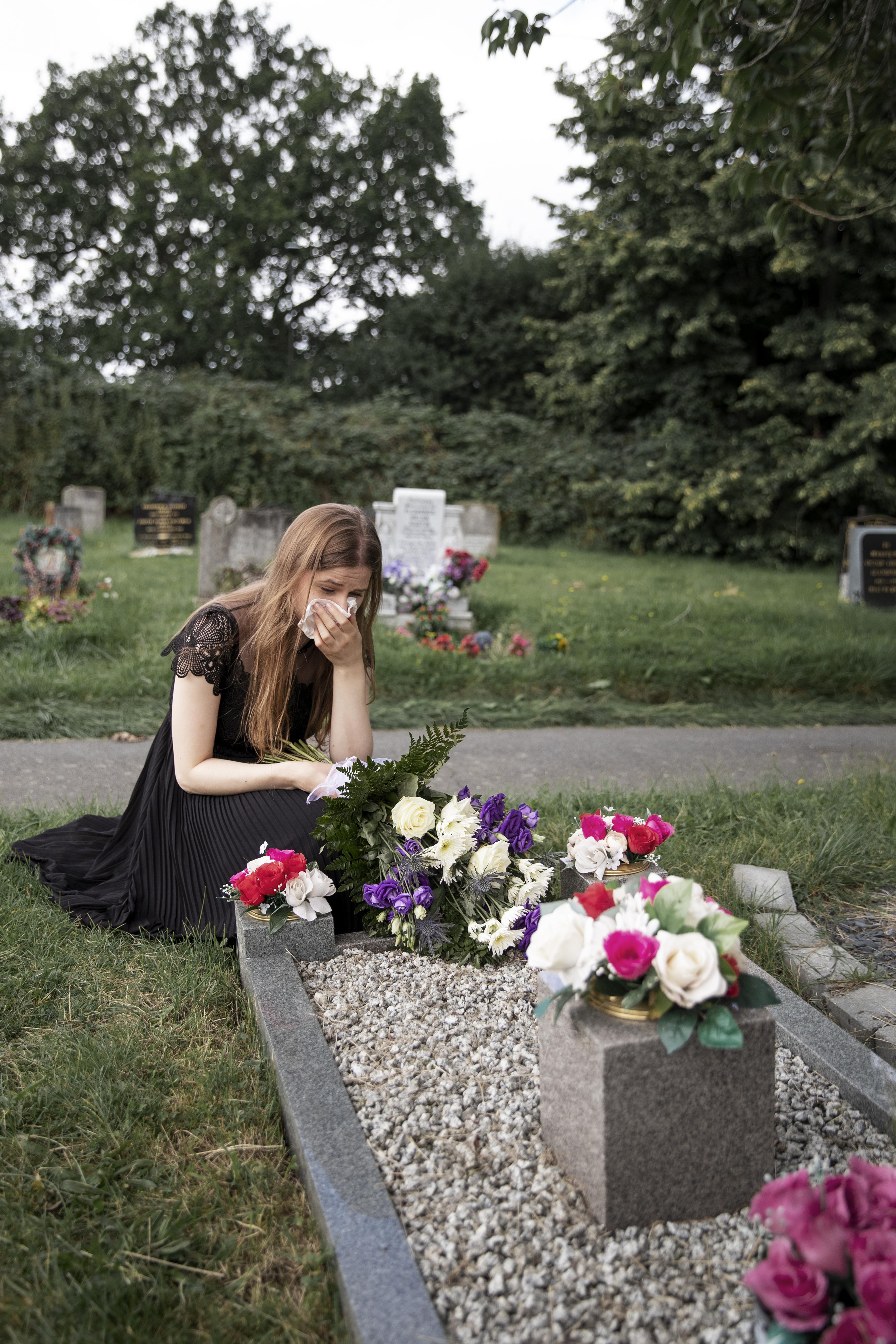 Una joven afligida ante una tumba en un cementerio | Fuente: Freepik