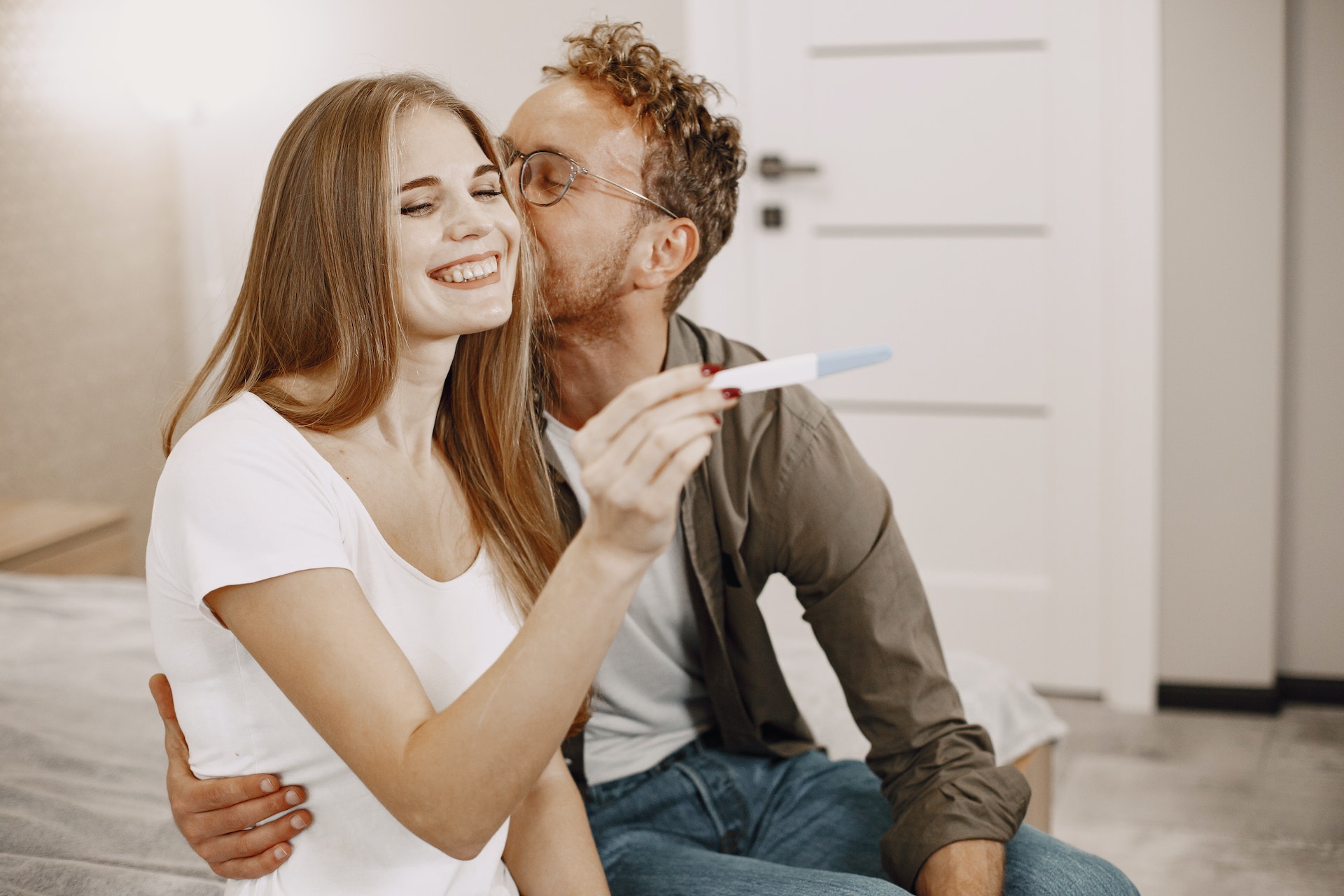 Una mujer sostiene un kit de prueba de embarazo mientras un hombre la besa. | Foto: Pexels