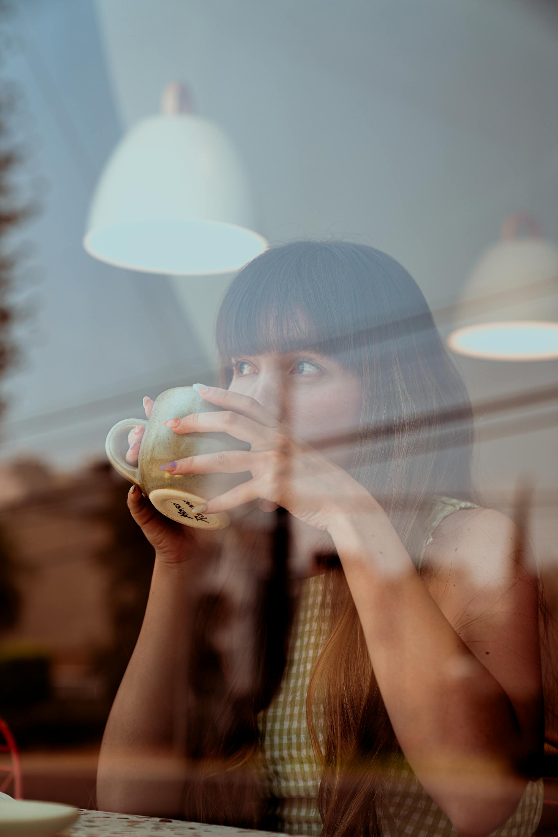 Una mujer bebiendo café y mirando por la ventana de la cafetería | Fuente: Pexels