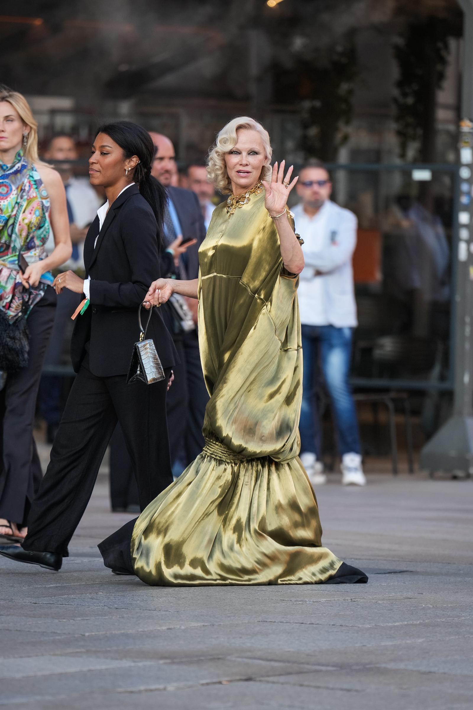 Anderson sonríe y saluda al llegar a Milán, mientras la tela vaporosa de su vestido metalizado se arrastra tras ella. Su aparición tuvo lugar durante la Semana de la Moda de Milán, en la temporada de moda femenina Primavera/Verano 2027. | Fuente: Getty Images