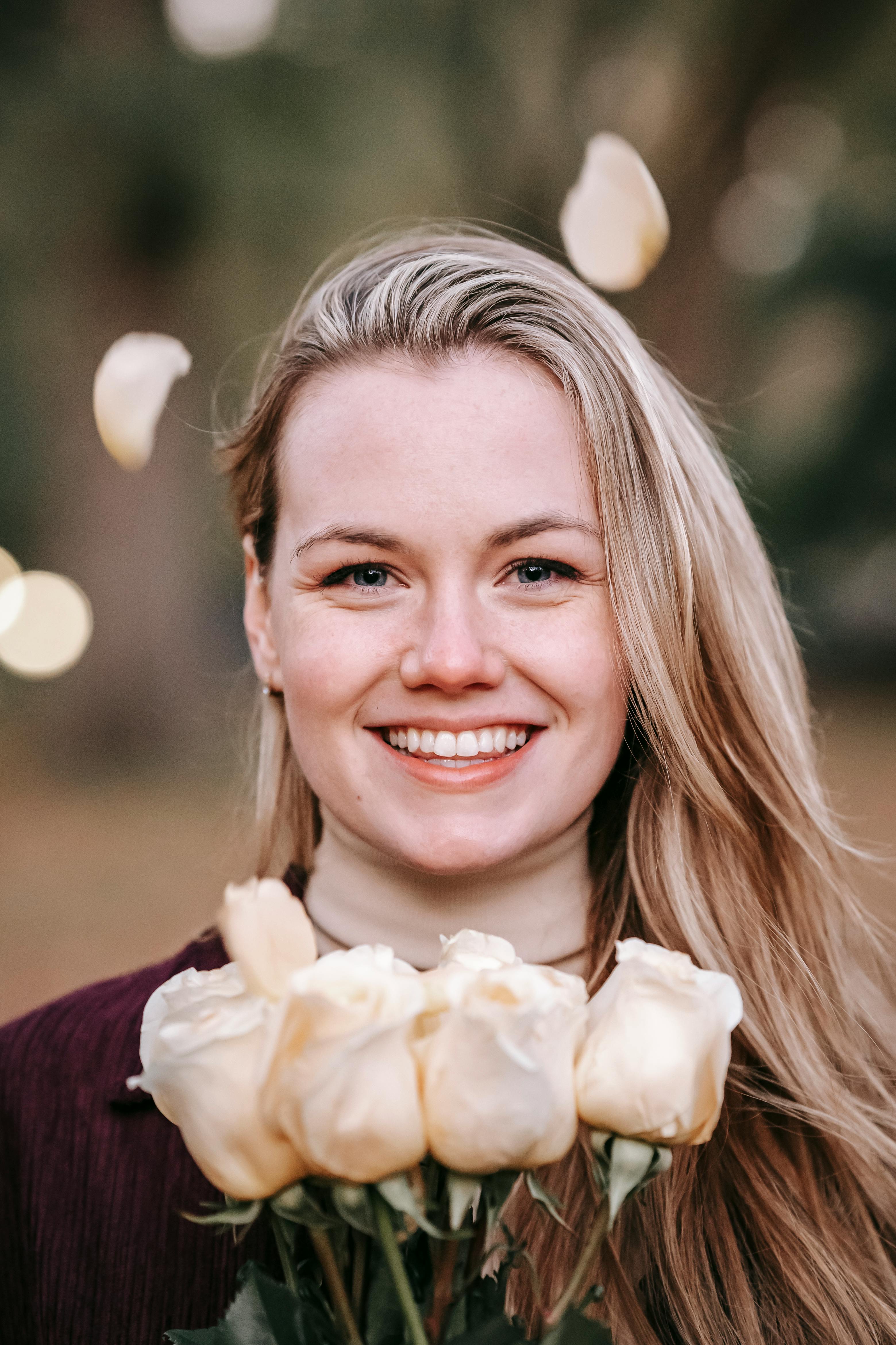 Mujer sonriente con ramo de rosas mirando a cámara | Foto: Pexels