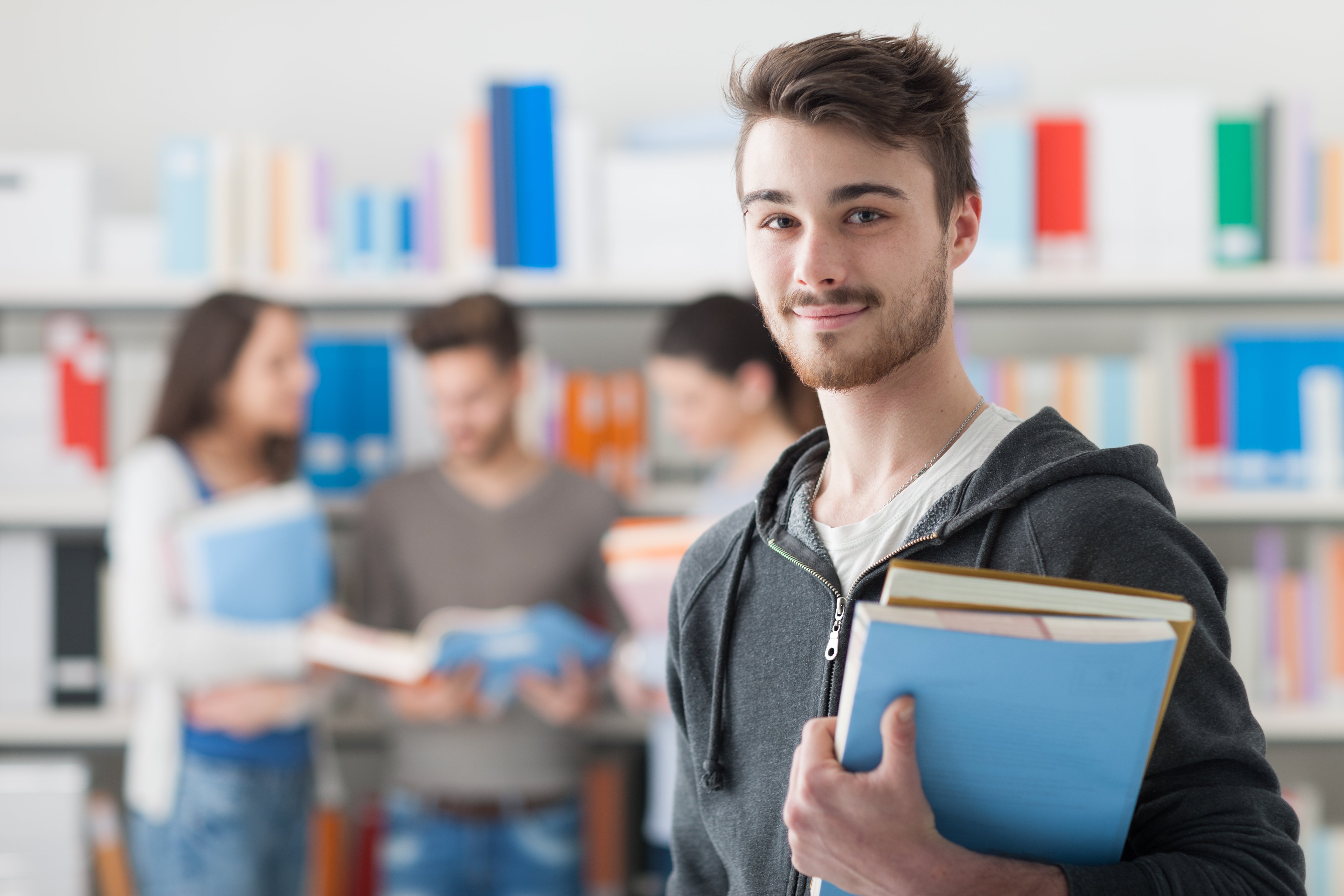 Estudiante sosteniendo libros y sonriendo a la cámara. Fuente: Shutterstock