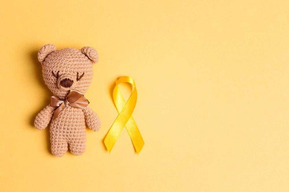 Oso tejido de juguete junto a la cinta dorada de concientización del cáncer infantil. | Foto: Shutterstock
