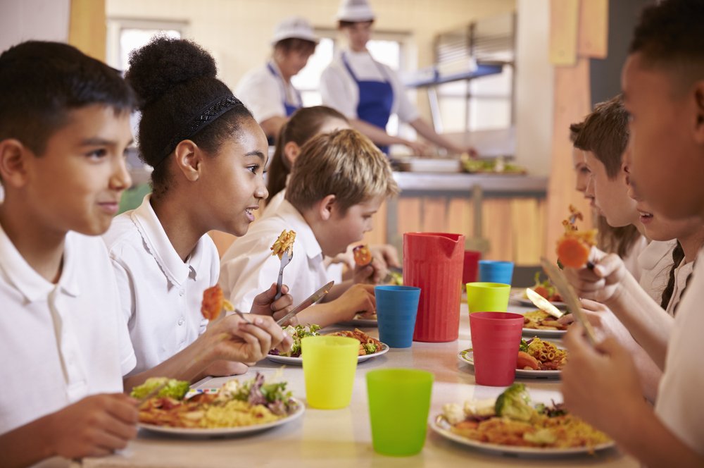 Niños de primaria almozando en la cafetería de la escuela. | Fuente: Shutterstock.