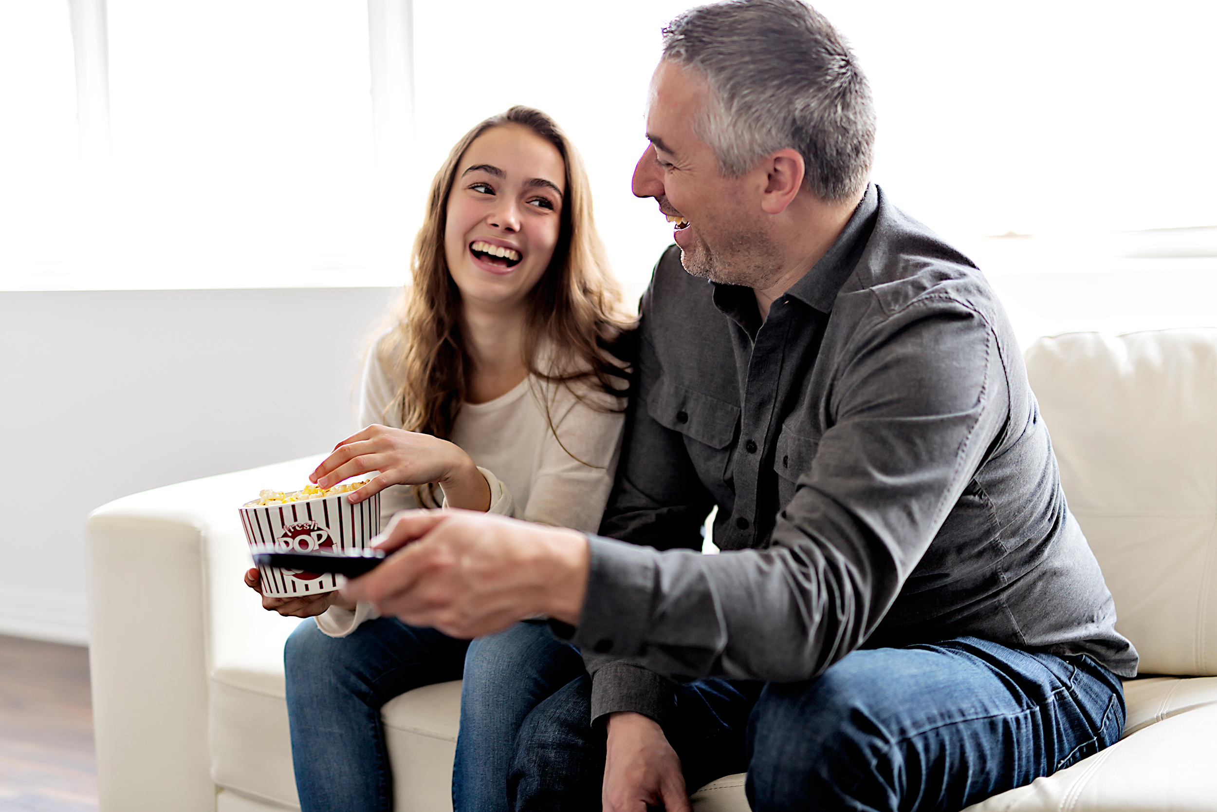 Un hombre mayor y una mujer más joven fotografiados riendo juntos mientras ven la tele y comen palomitas | Foto: Shutterstock