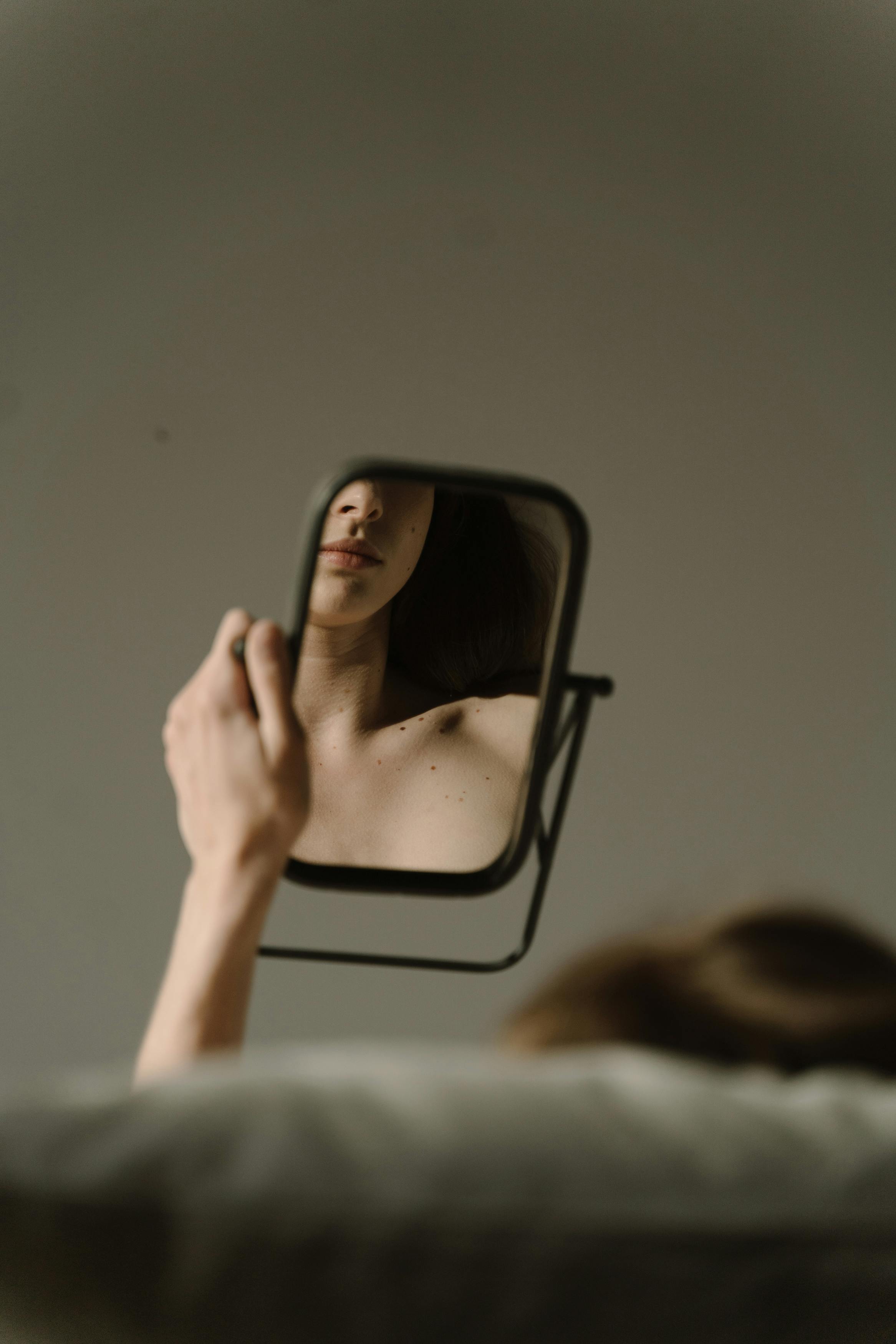Mujer sentada en un sofá mirando su reflejo en un espejo | Fuente: Pexels