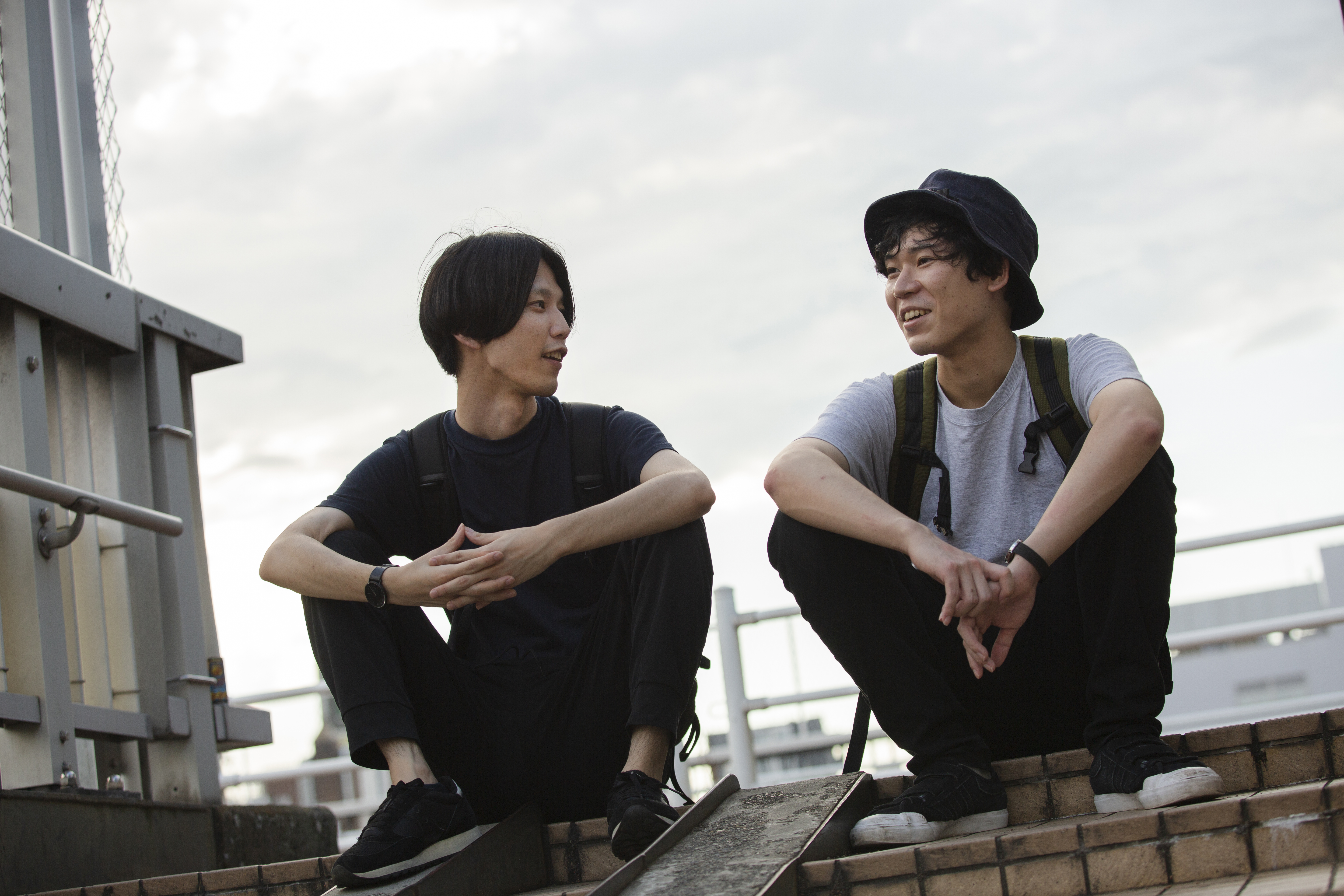 Dos jóvenes asiáticos sentados en un tejado, hablando | Foto: Getty Images