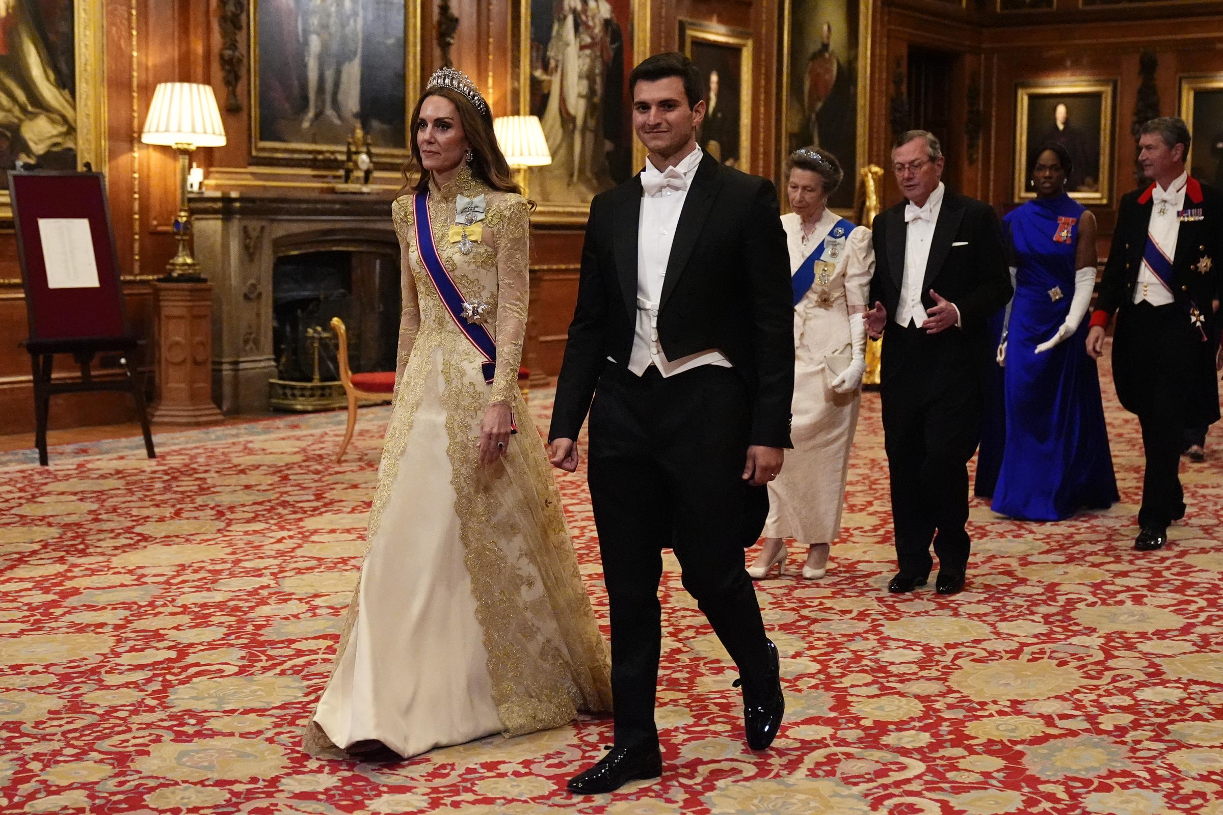 Catherine, princesa de Gales, camina junto a Michael Boulos durante la procesión hacia el banquete de Estado en el castillo de Windsor el 17 de septiembre de 2025, en honor al presidente estadounidense Donald Trump y la primera dama Melania Trump. Catherine deslumbra con un vestido de encaje marfil y dorado, mangas largas transparentes y elaborados bordados dorados, junto con la tiara Lover's Knot de la reina Mary, la banda de la Real Orden Victoriana y la Orden de la Familia Real del rey Charles III. Boulos viste un elegante frac negro y corbata blanca. | Fuente: Getty Images