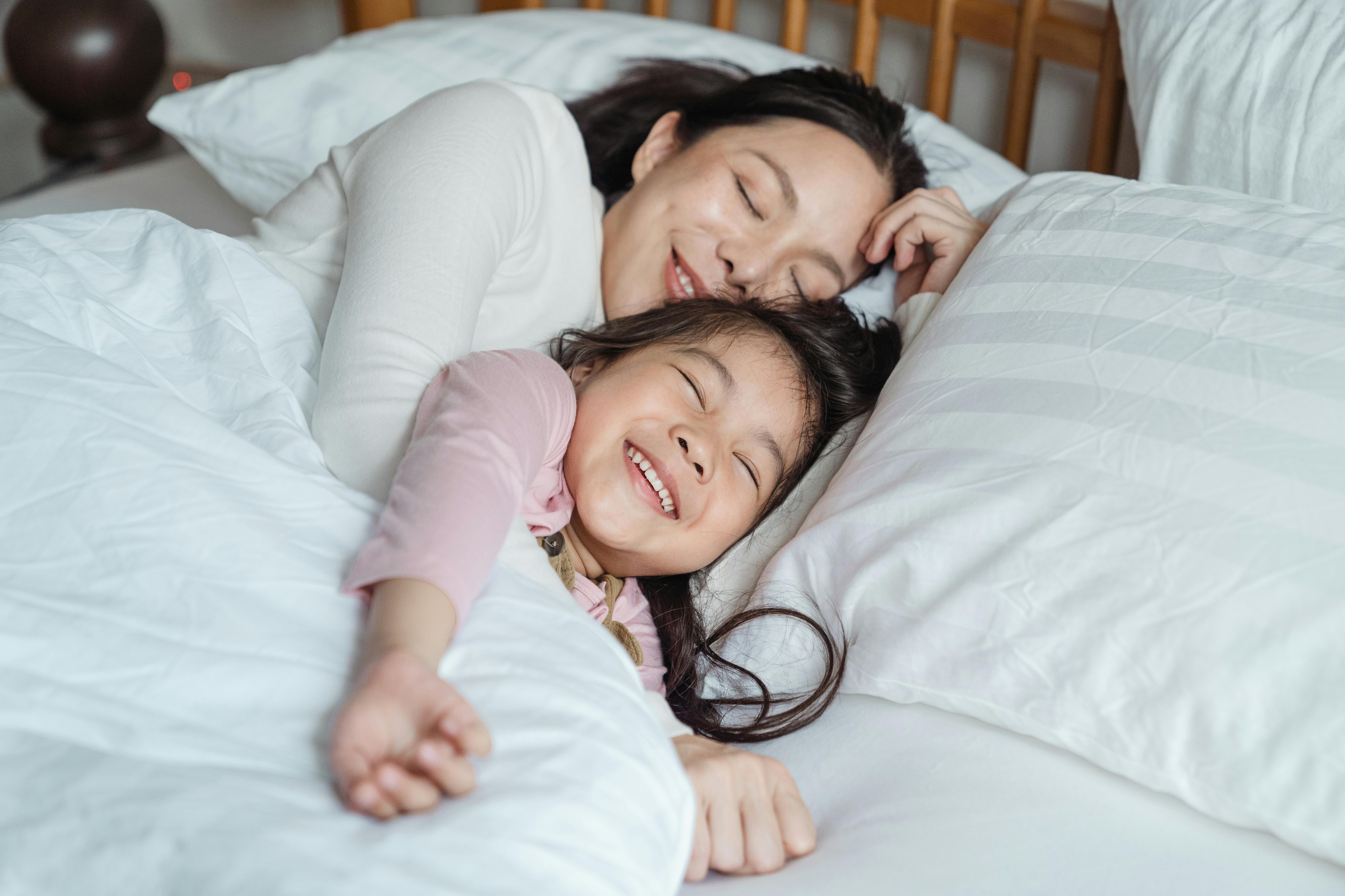 Madre e hija sonríen en la cama | Foto: Pexels