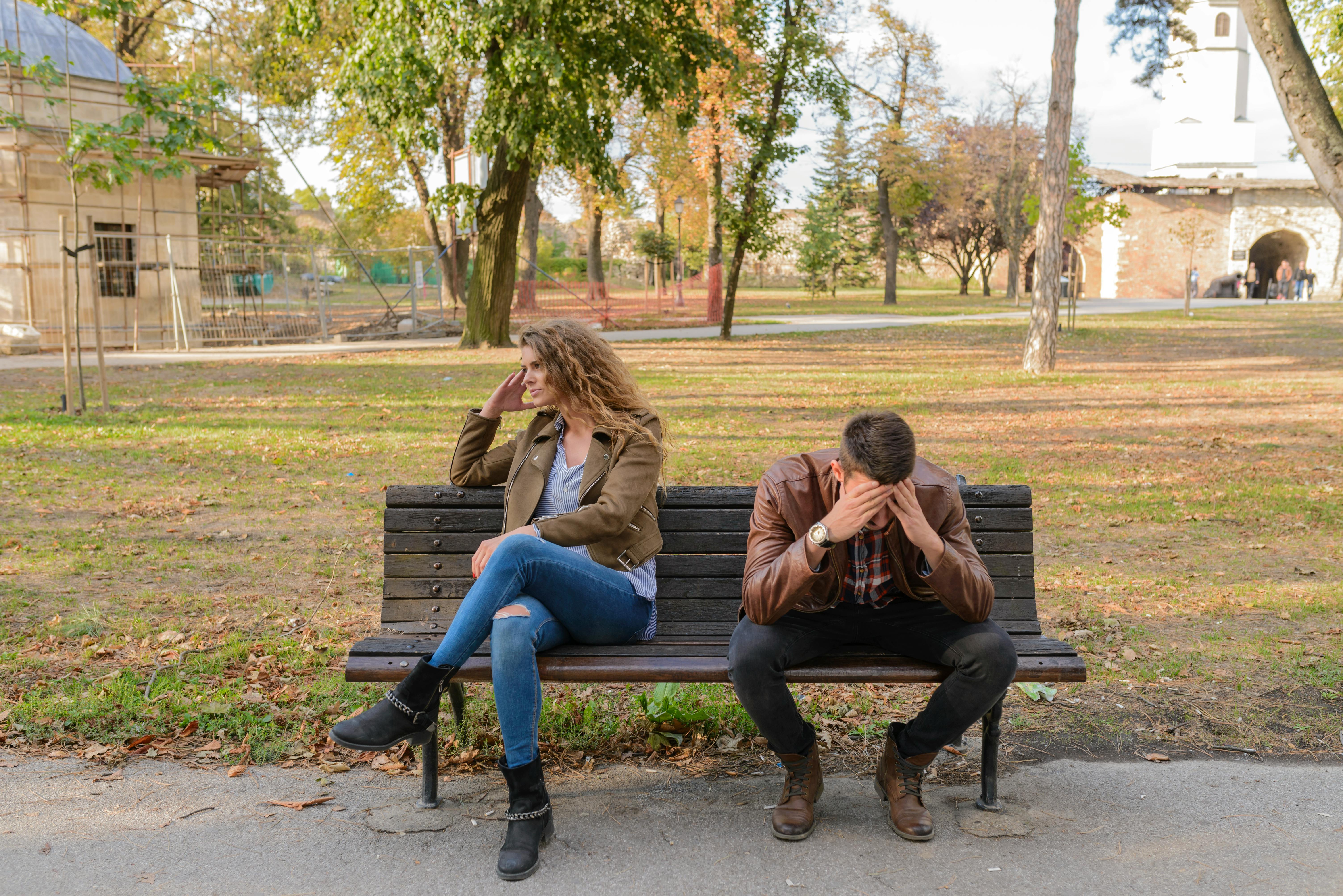 Una mujer enfadada sentada junto a un hombre que llora en un banco del parque | Fuente: Pexels