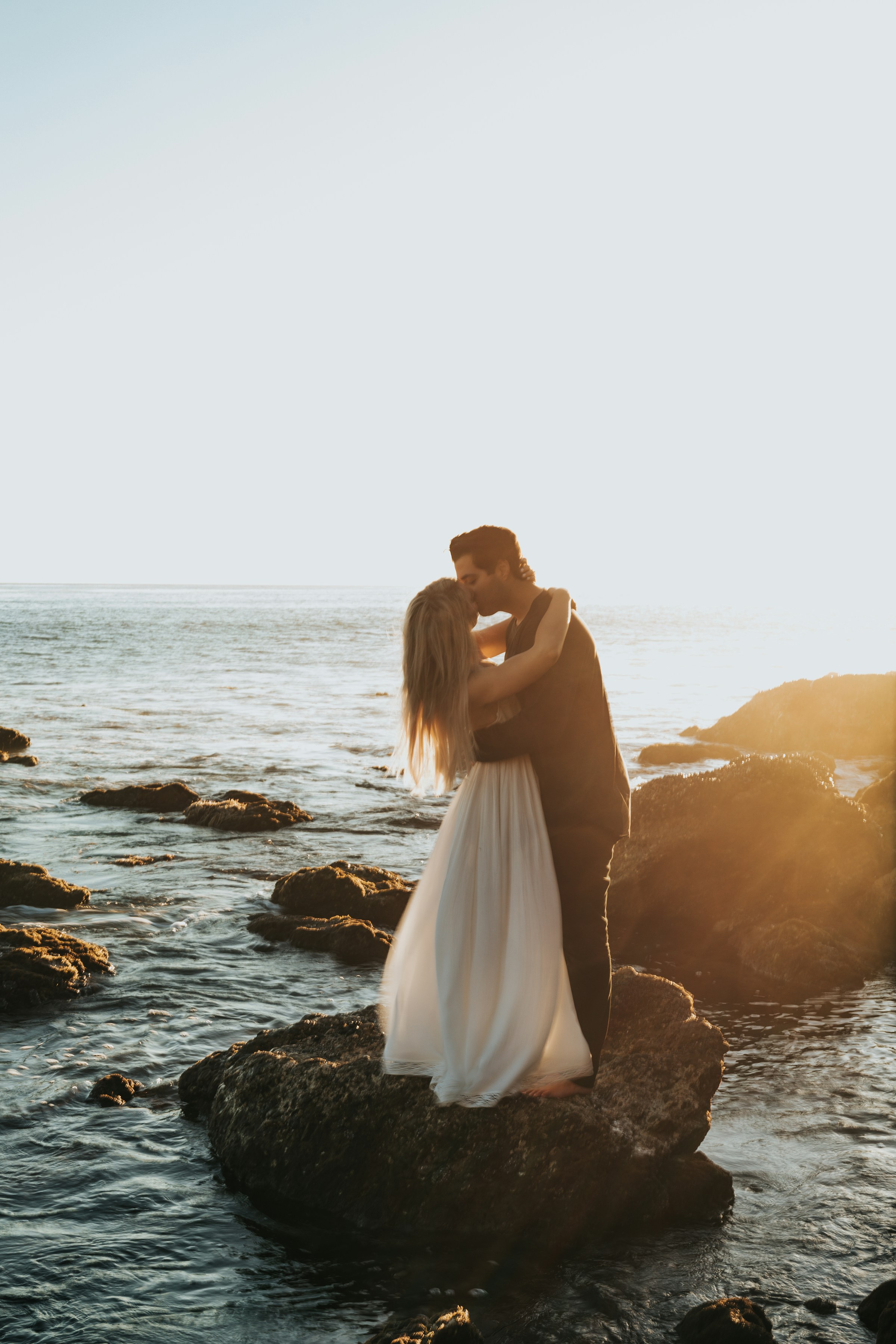 Una pareja besándose encima de una roca en una playa | Fuente: Unsplash