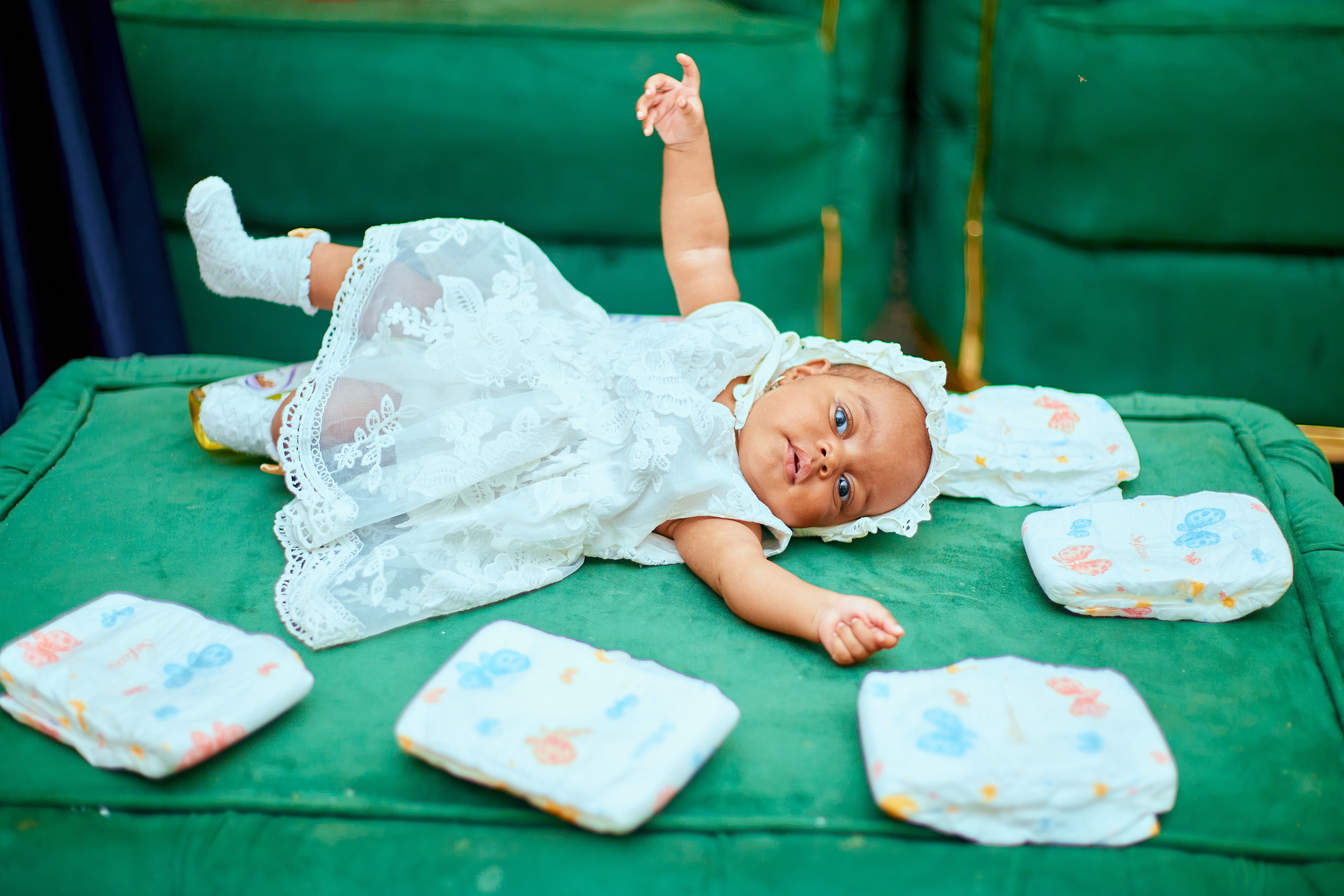 Una bambina carinissima con un vestitino bianco che gioca su un divano verde | Fonte: Pexels