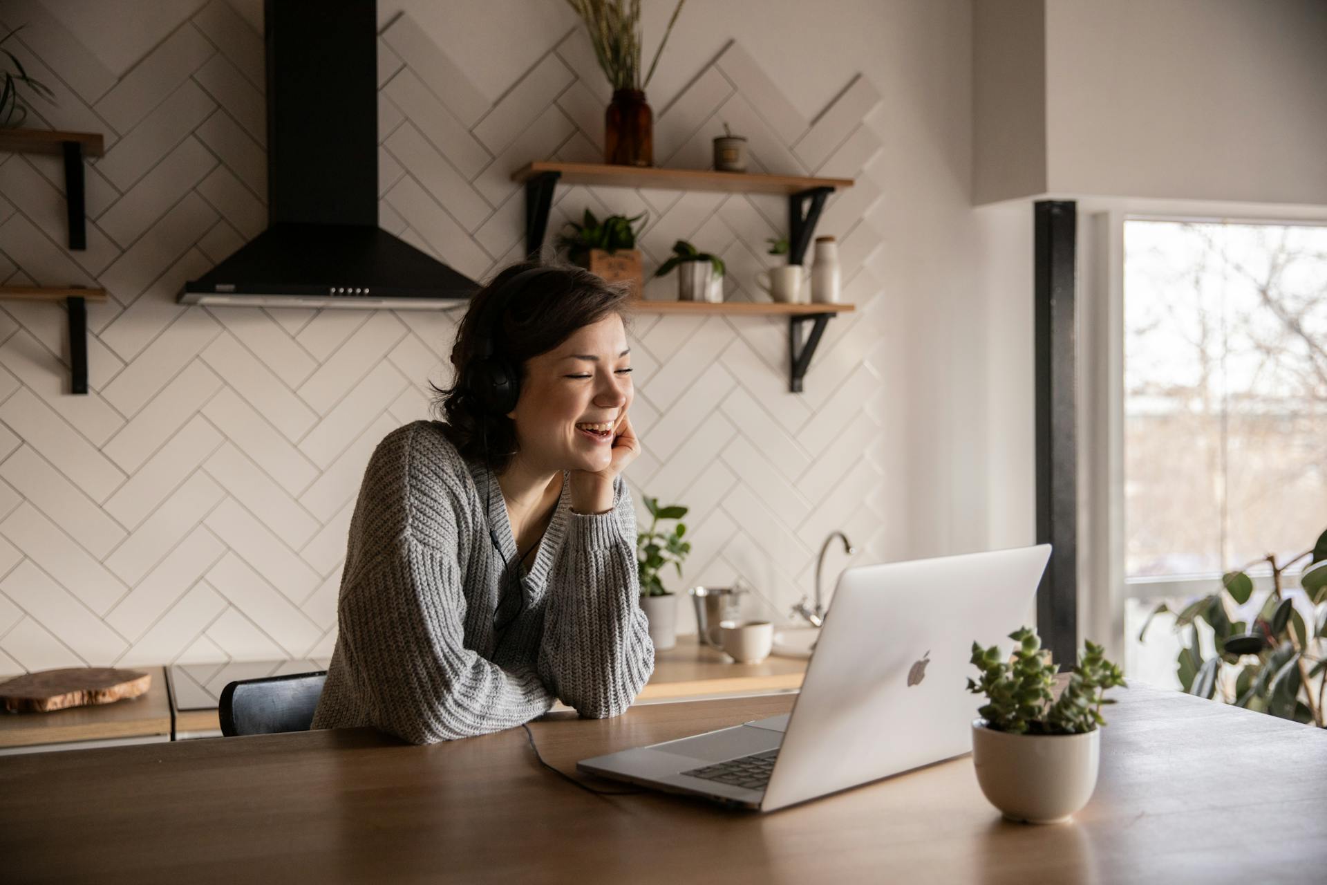 Una mujer sonriente hablando a través de un ordenador portátil mientras está sentada en la cocina | Fuente: Pexels