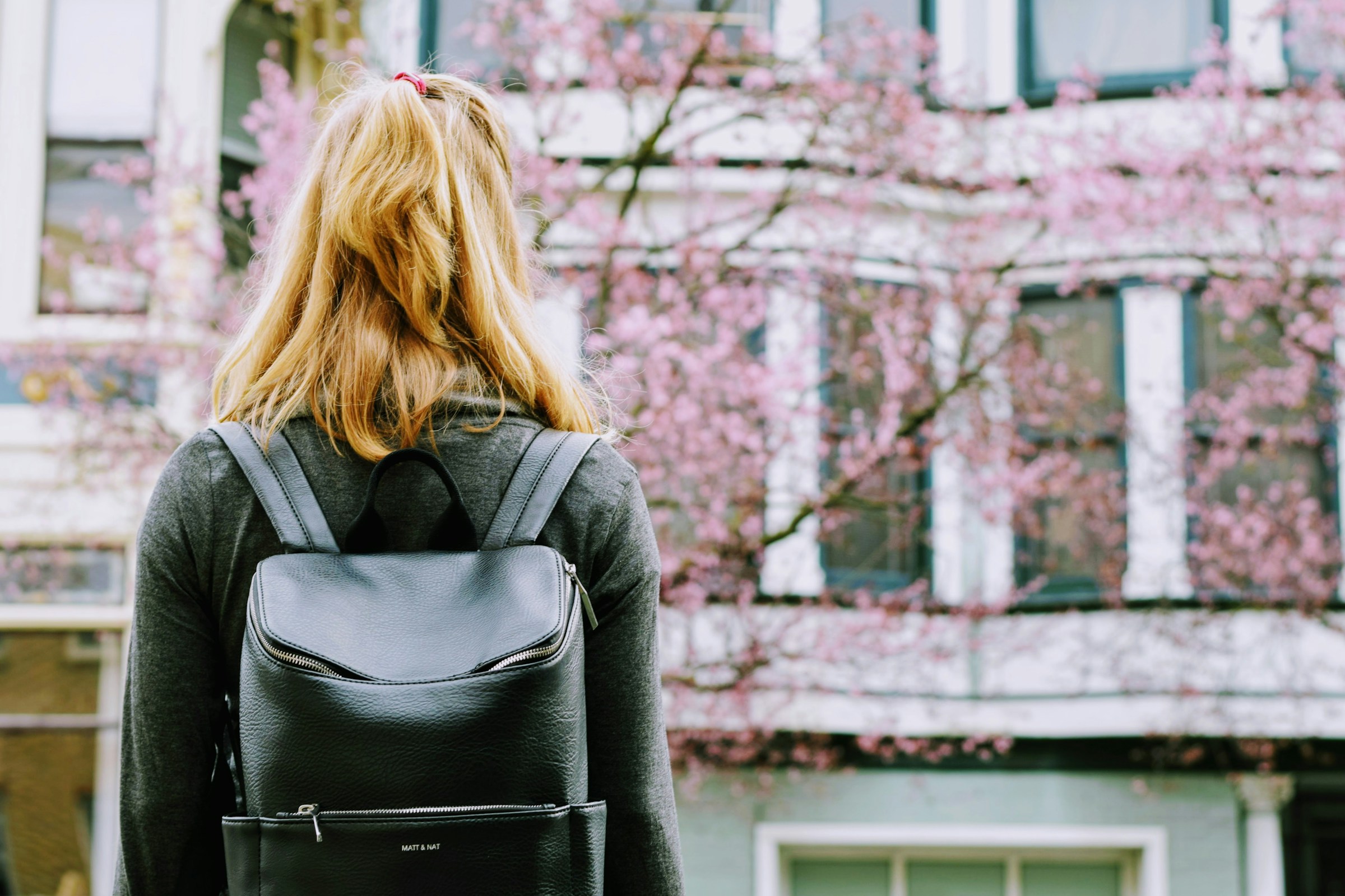 Vista posterior de una joven con una mochila delante de un edificio | Fuente: Unsplash