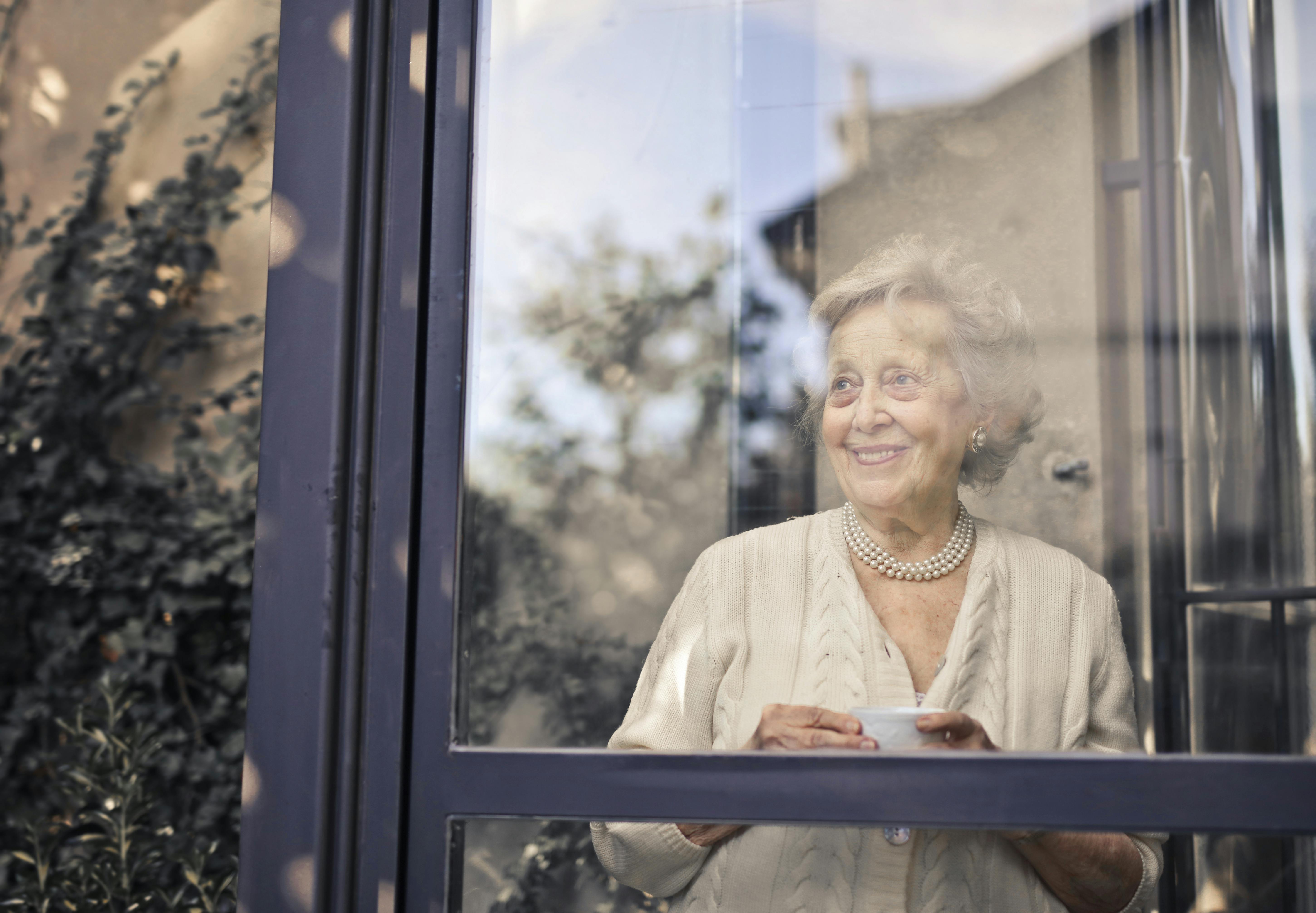 Una anciana sonriente mirando por la ventana | Fuente: Pexels