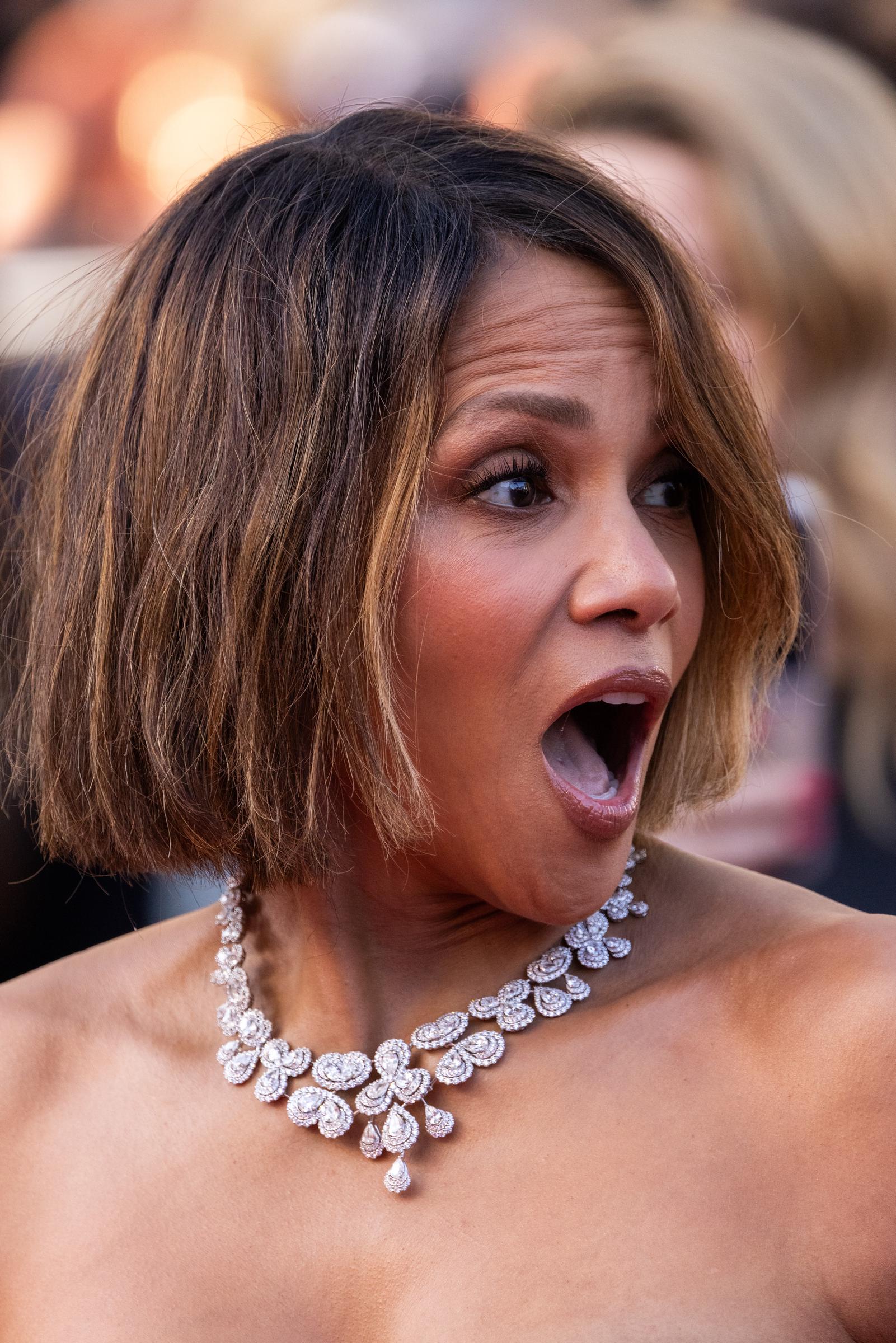 Halle Berry reacciona con expresión sorprendida en la alfombra roja de Cannes. Su glamuroso look incluía un suave maquillaje neutro, voluminosas pestañas y un elegante corte recto hasta la barbilla con sutiles reflejos.