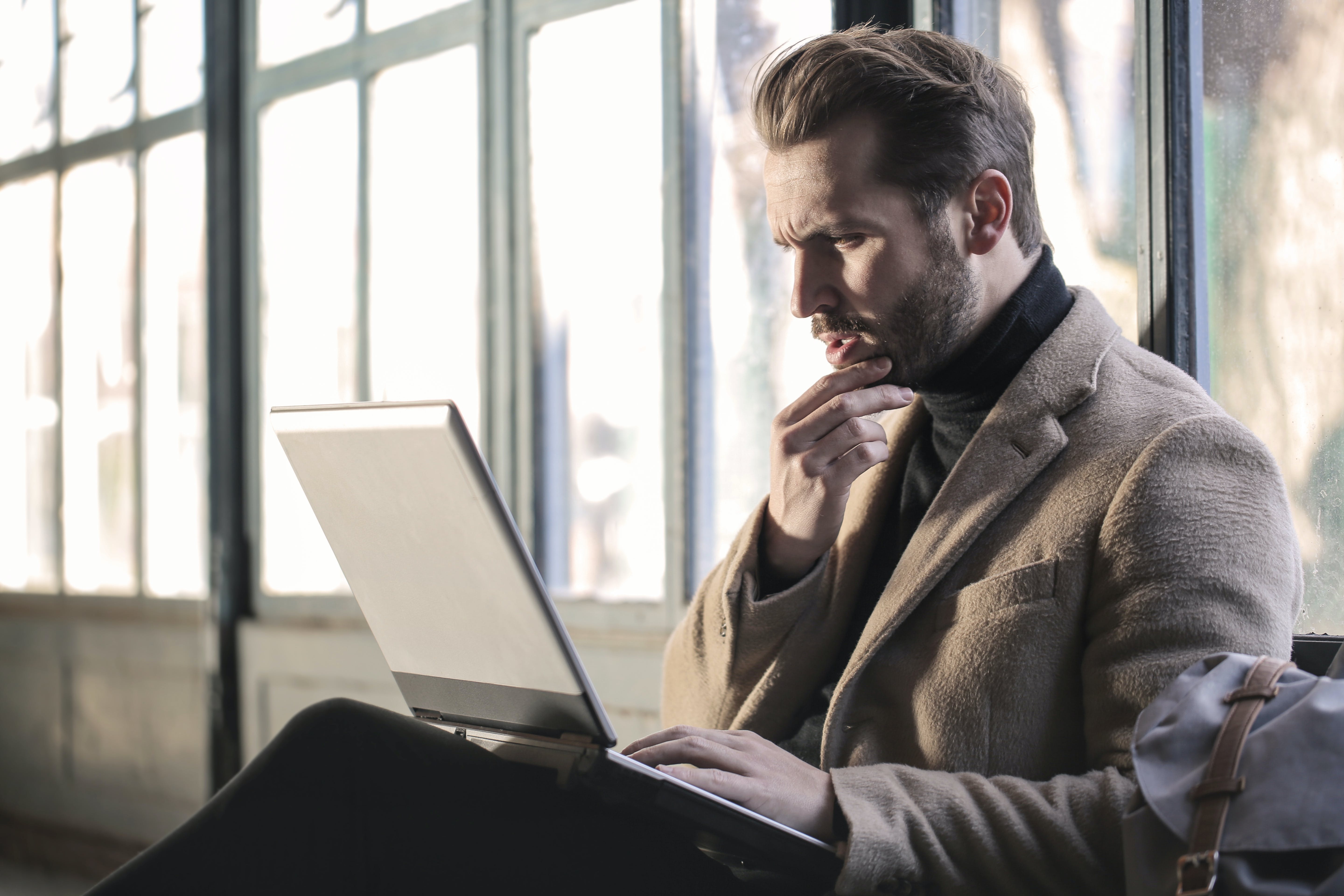 Un hombre confuso se sujeta la barbilla mientras está sentado mirando un portátil | Foto: Pexels
