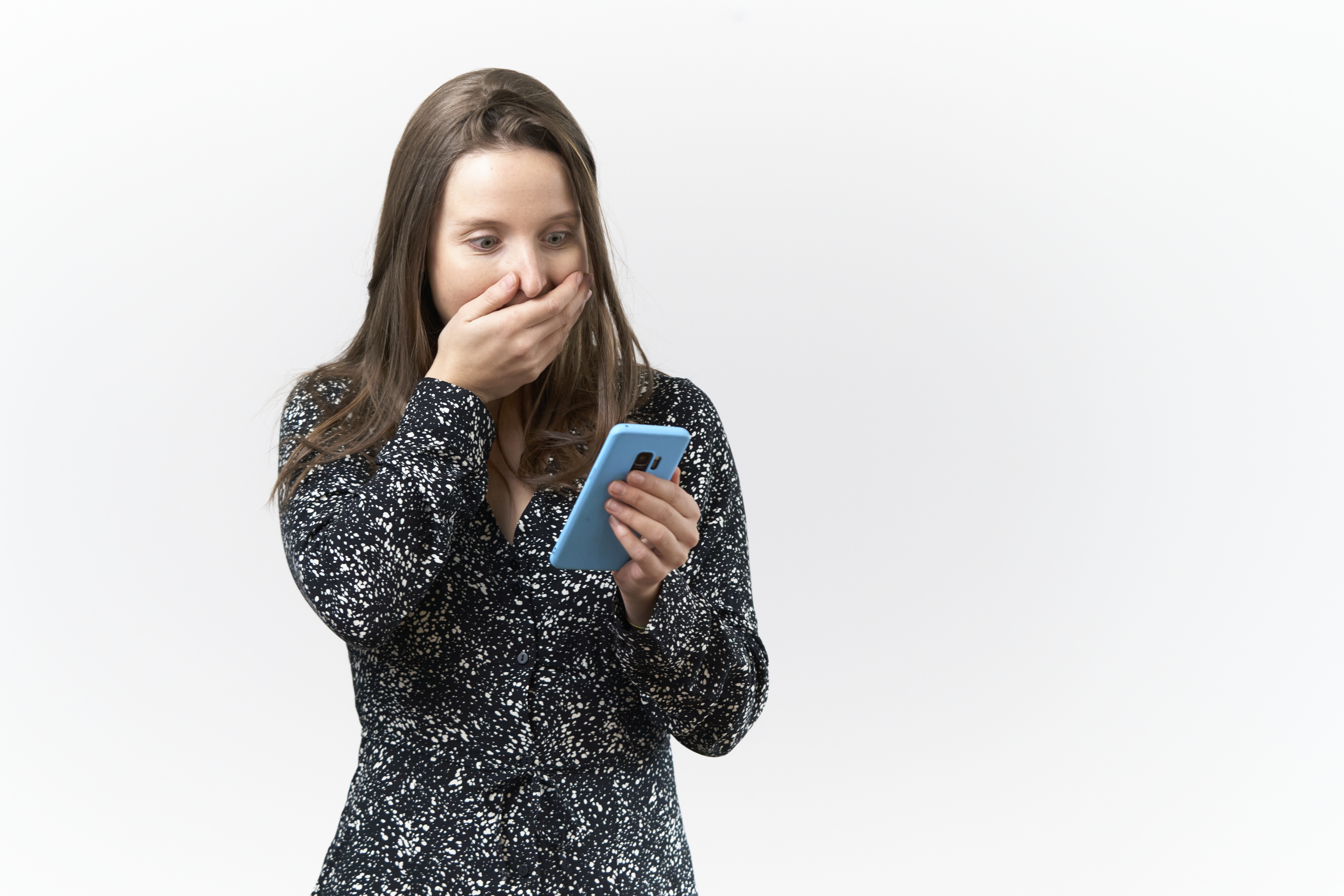 Mujer joven con expresión sorprendida leyendo mensajes en el móvil sobre fondo blanco | Foto: Getty Images