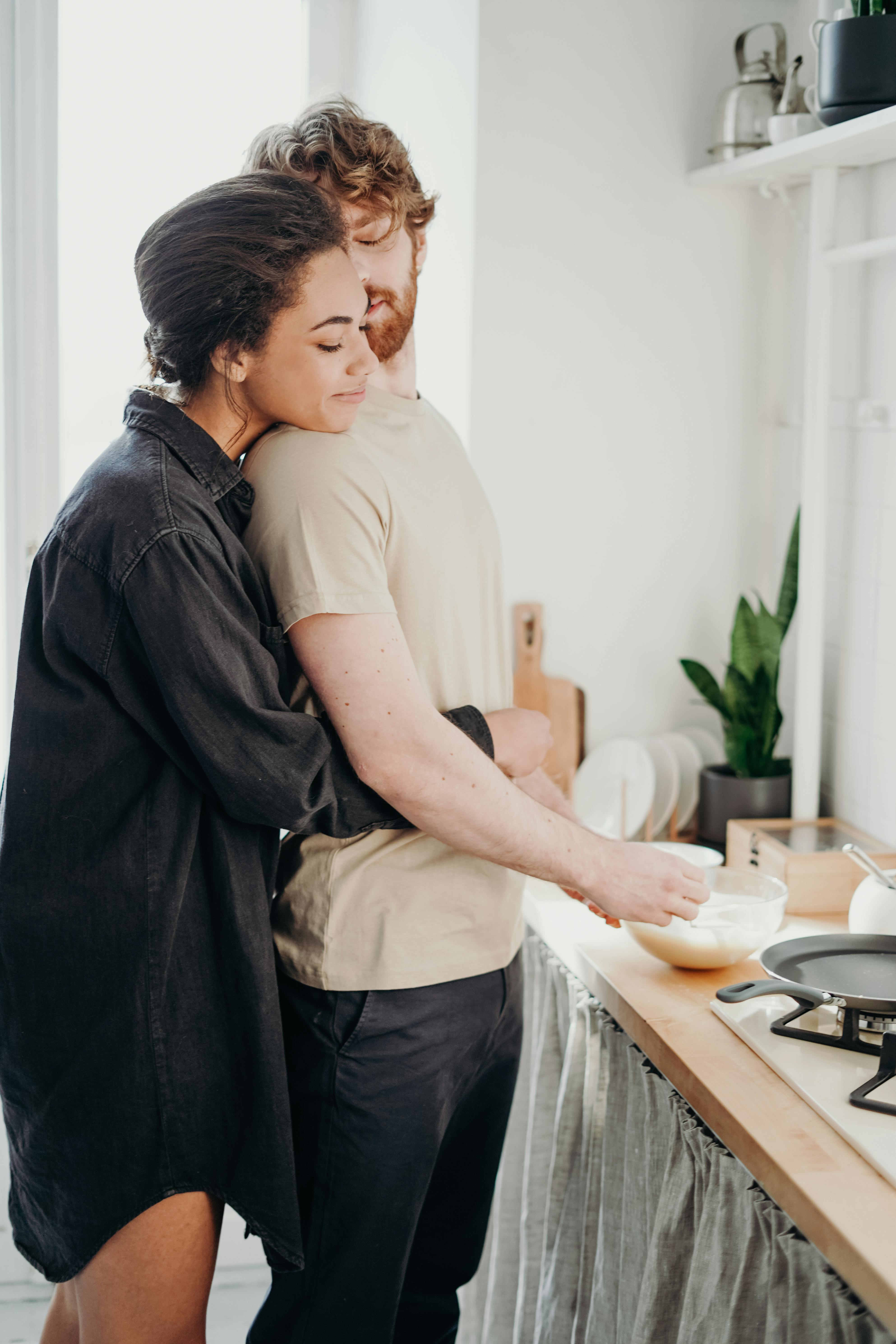Pareja se abraza mientras el hombre cocina | Foto: Pexels