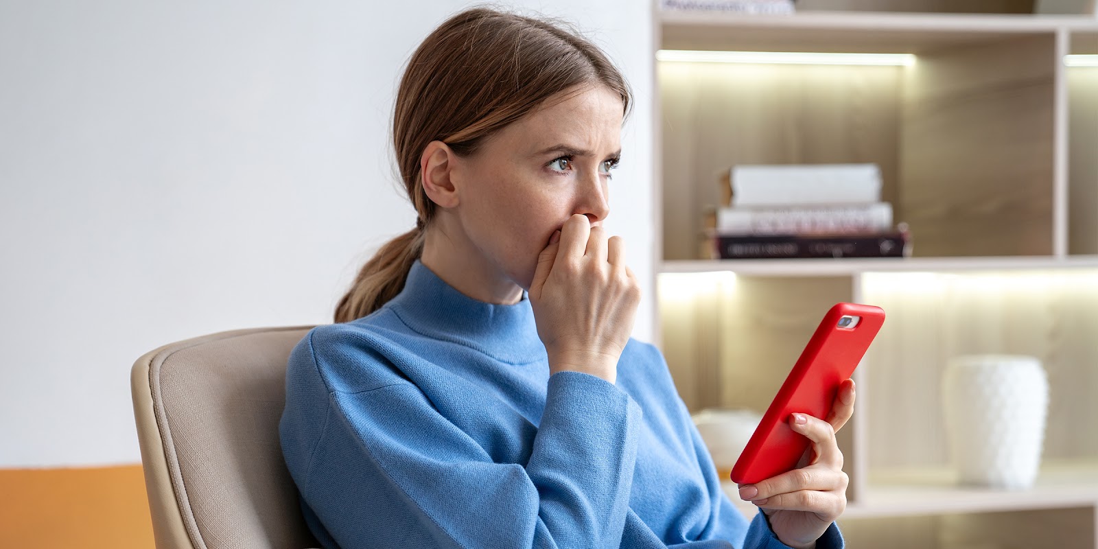 Una mujer pensativa sentada con un teléfono en la mano | Fuente: Shutterstock