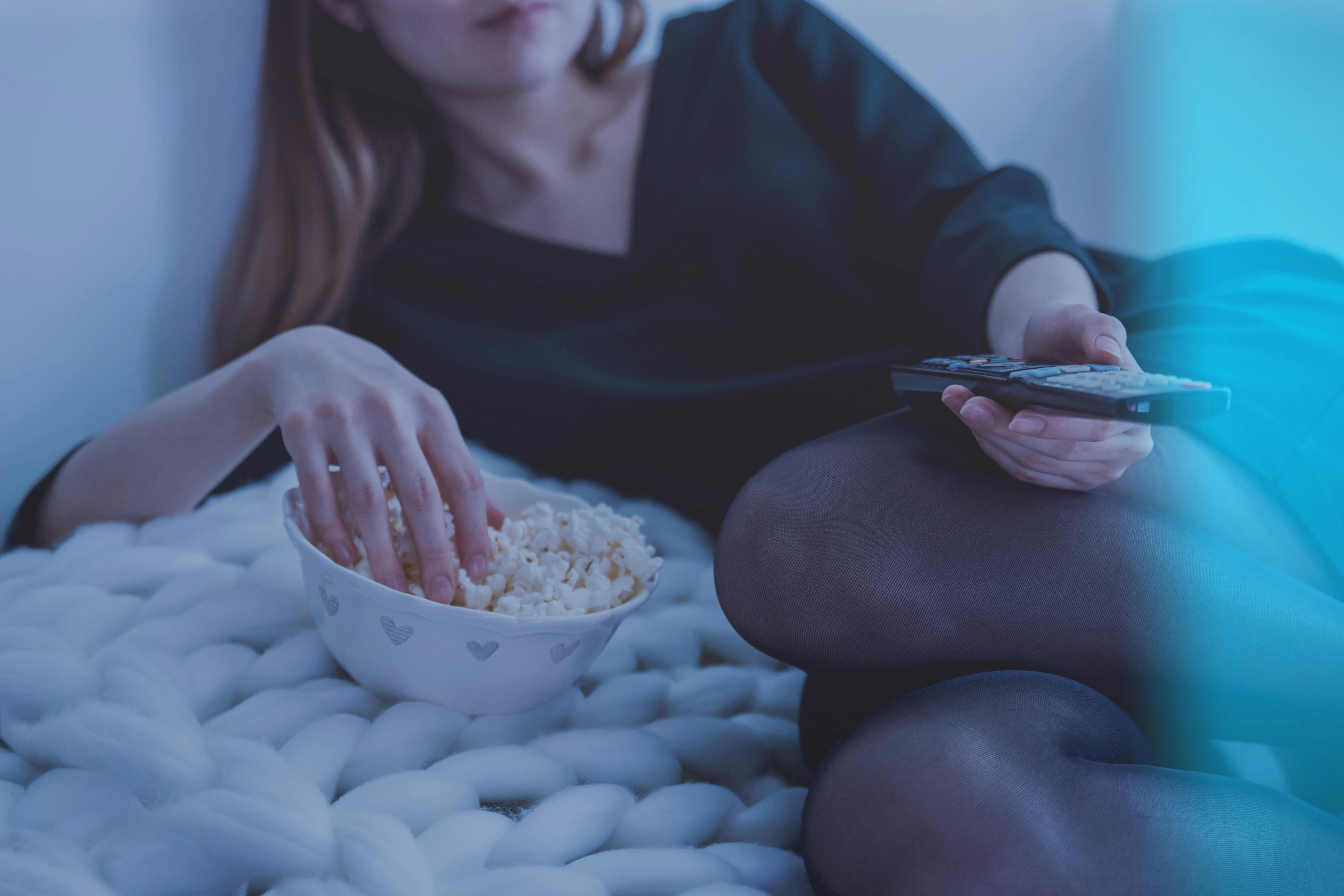 Una mujer sostiene un mando a distancia mientras come palomitas | Fuente: Pexels