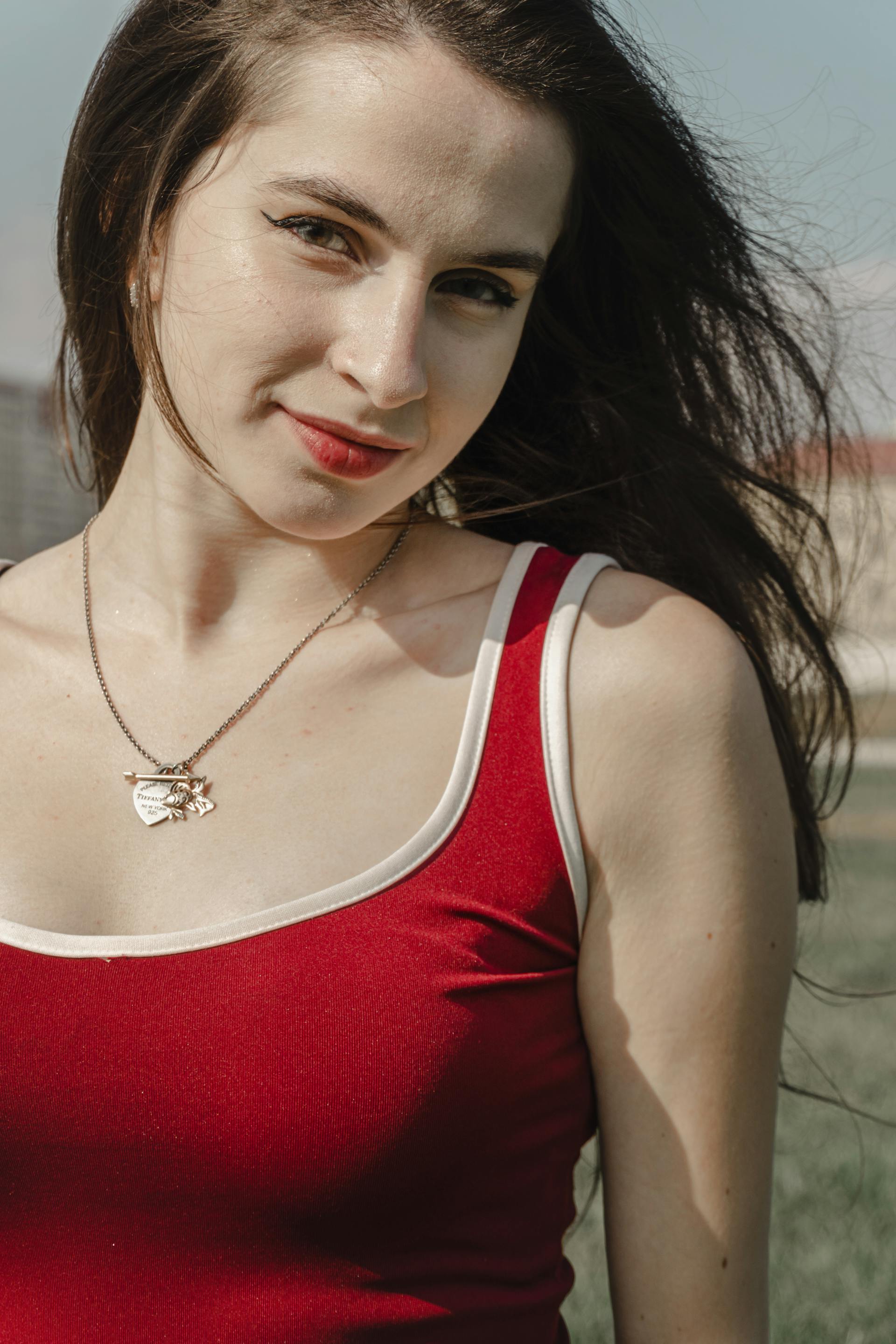 Una donna con un top rosso che sorride mentre si trova all'aperto | Fonte: Pexels