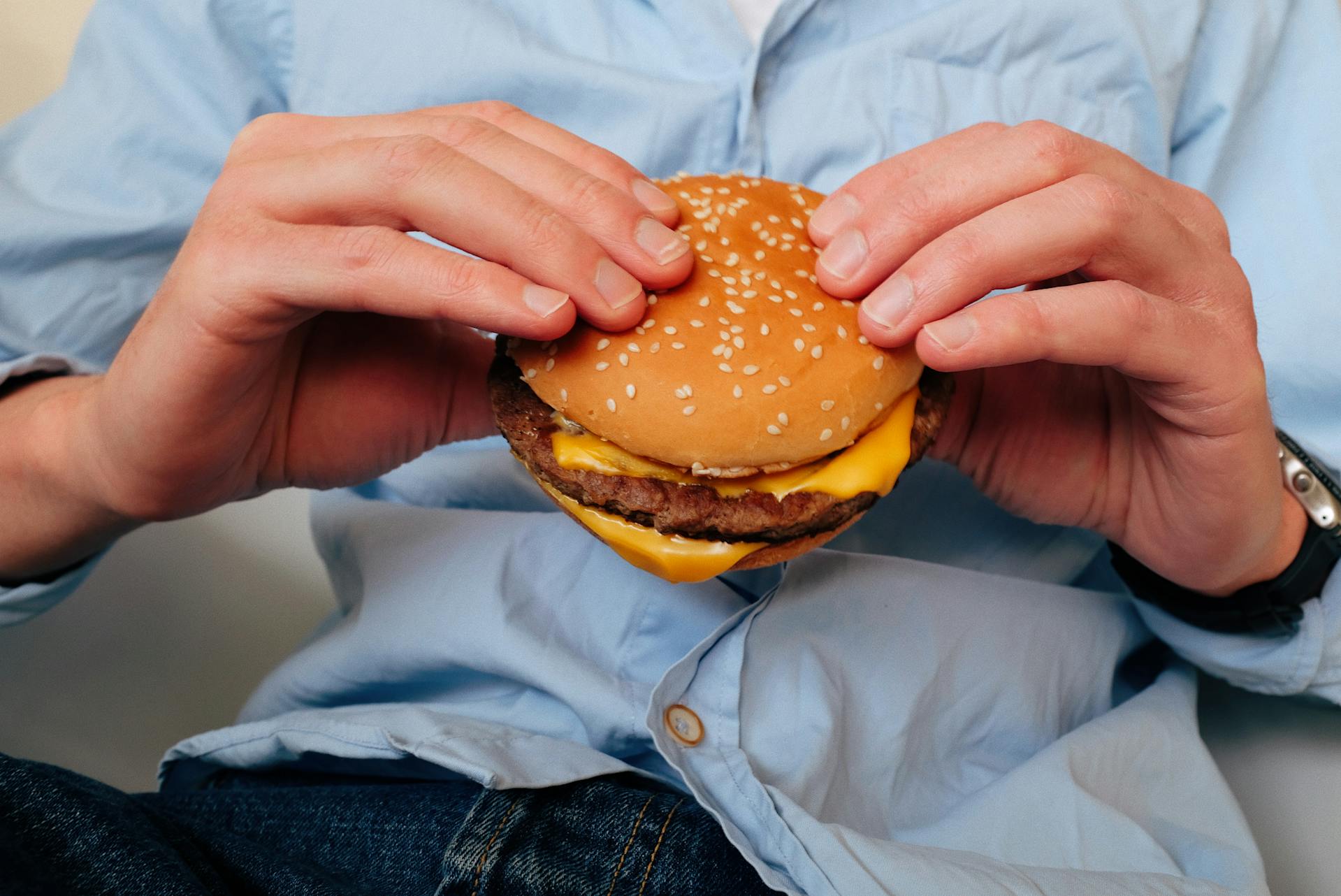Primer plano recortado de un hombre sujetando una hamburguesa | Fuente: Pexels