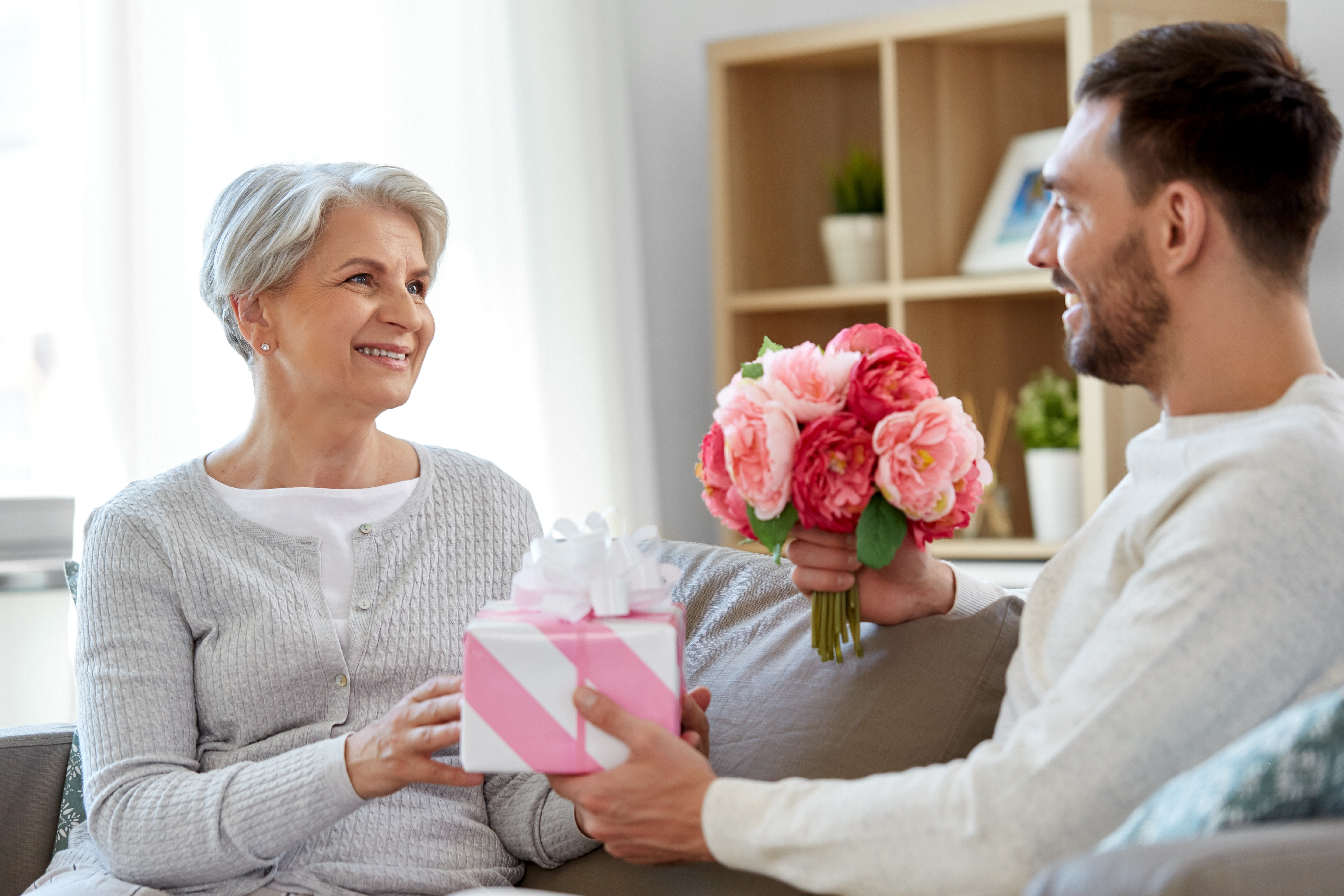Un hijo adulto sonriente dando un regalo y flores a su madre mayor. | Foto: Shutterstock