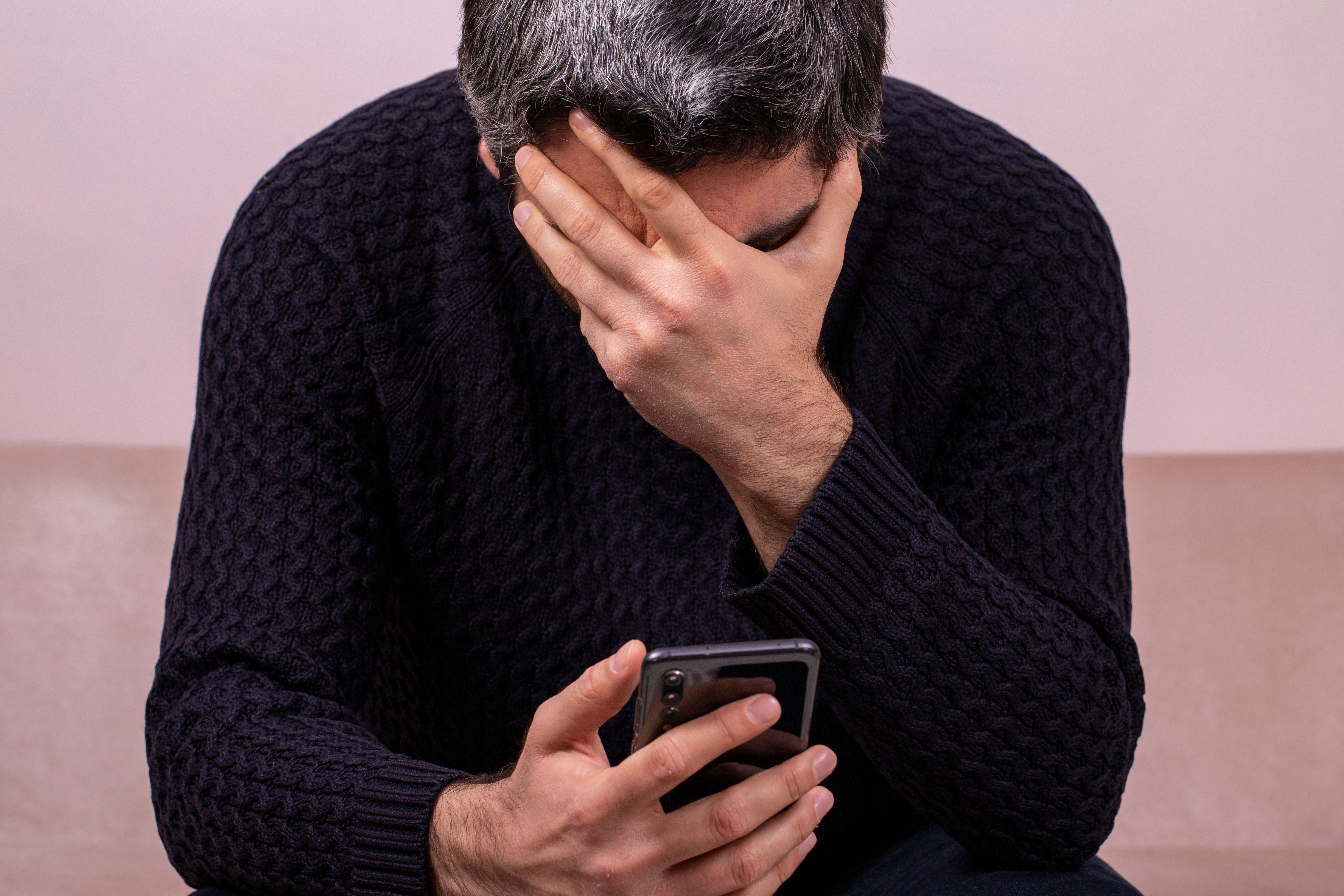 Hombre triste de mediana edad con el teléfono en la mano. | Fuente: Shutterstock