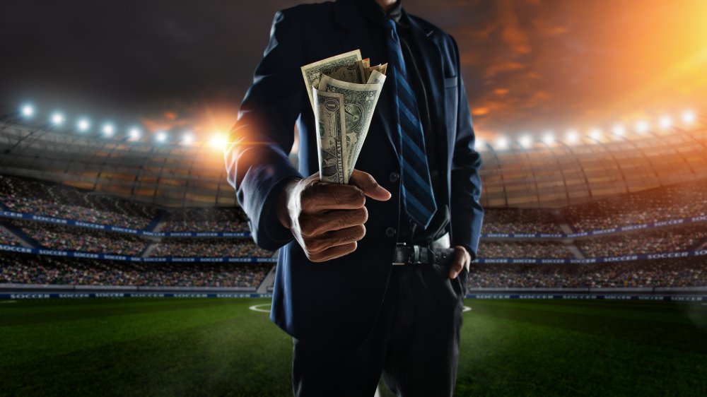 empresario sostiene una gran cantidad de billetes en el estadio de fútbol en segundo plano. I Foto: Shutterstock