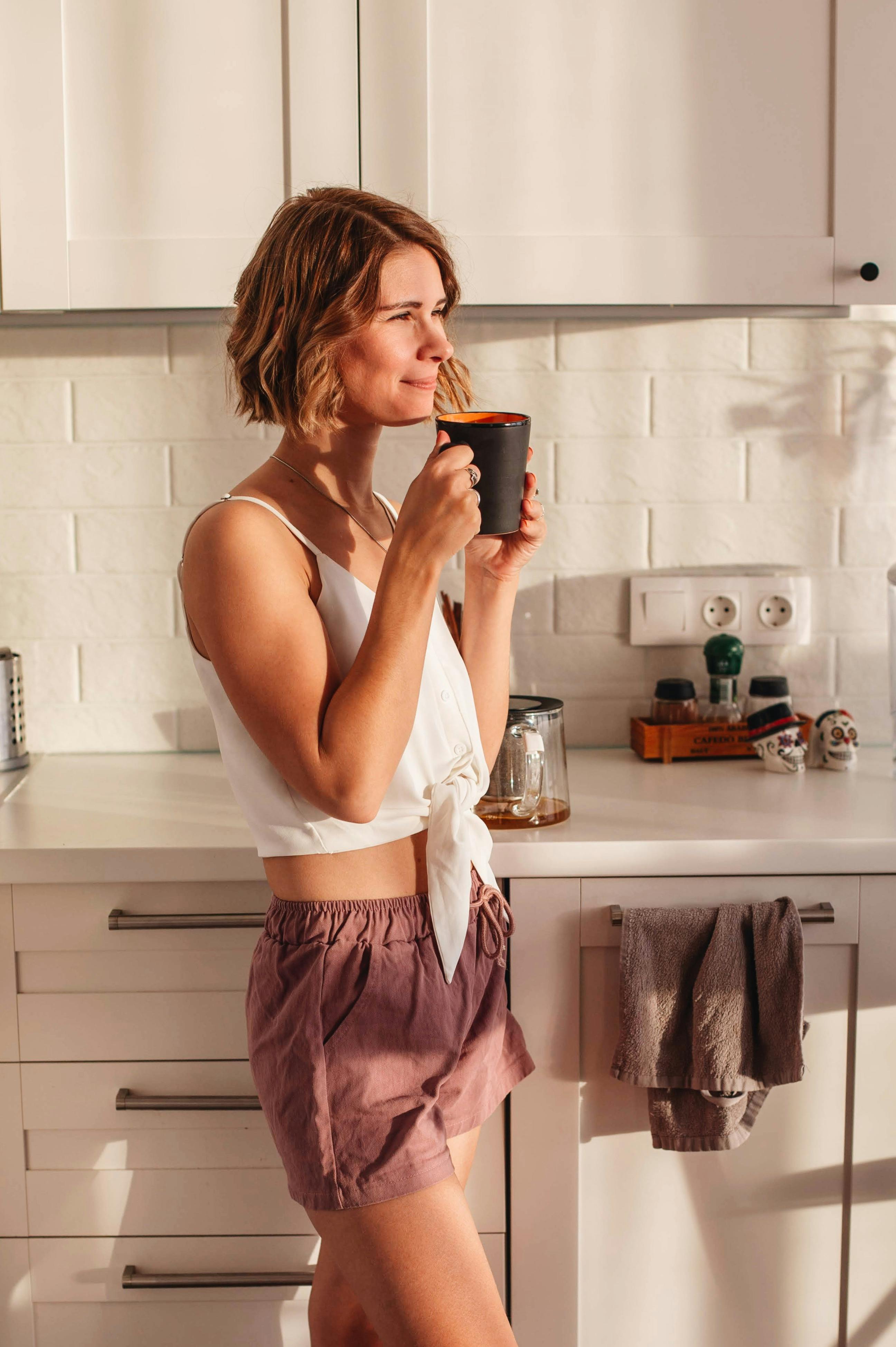 Una mujer feliz con una taza de café en la cocina | Fuente: Pexels