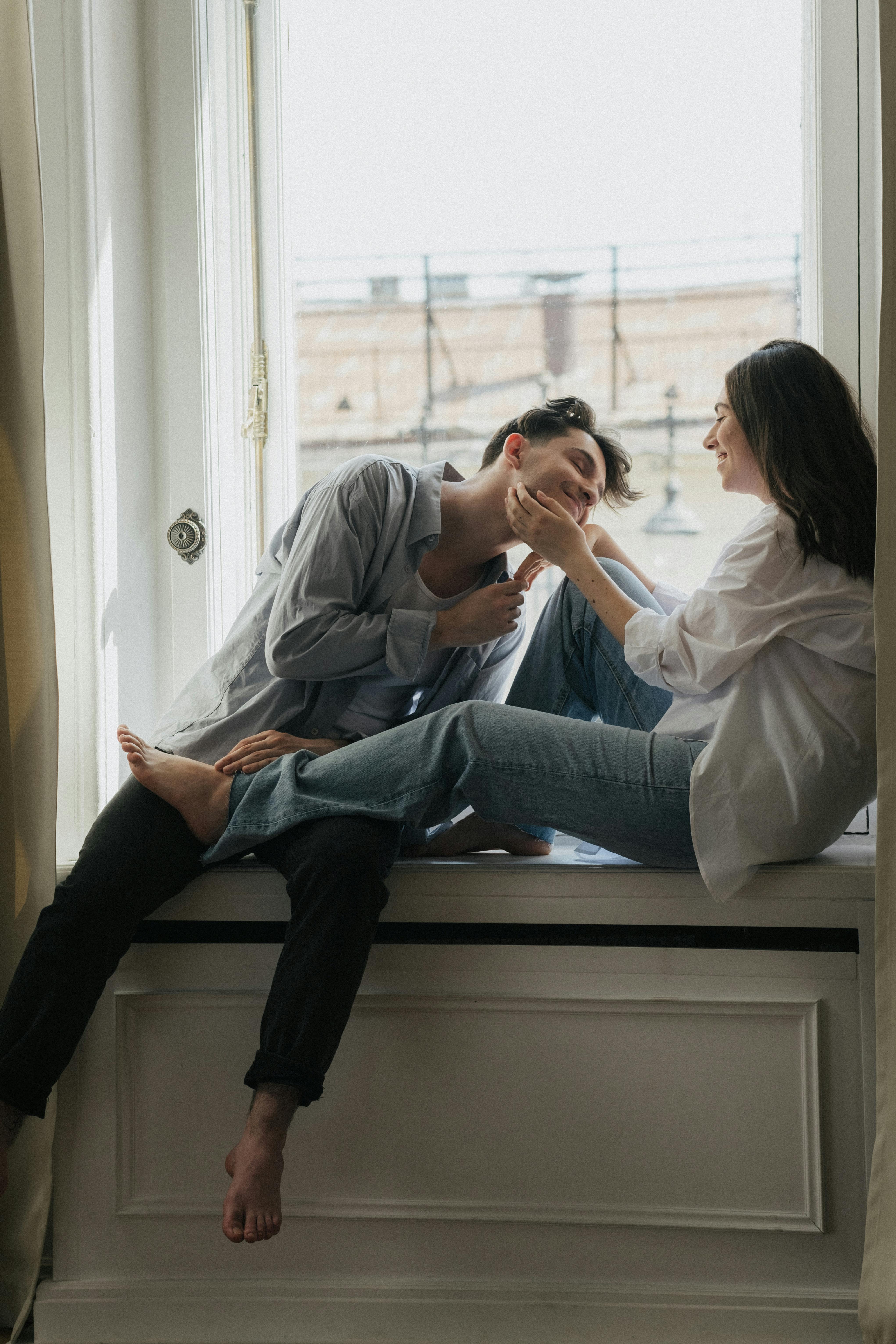 Una pareja feliz pasando el rato en el alféizar de una ventana | Fuente: Pexels