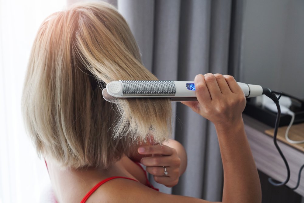 Mujer alisándose el cabello con una plancha. | Foto: Shutterstock