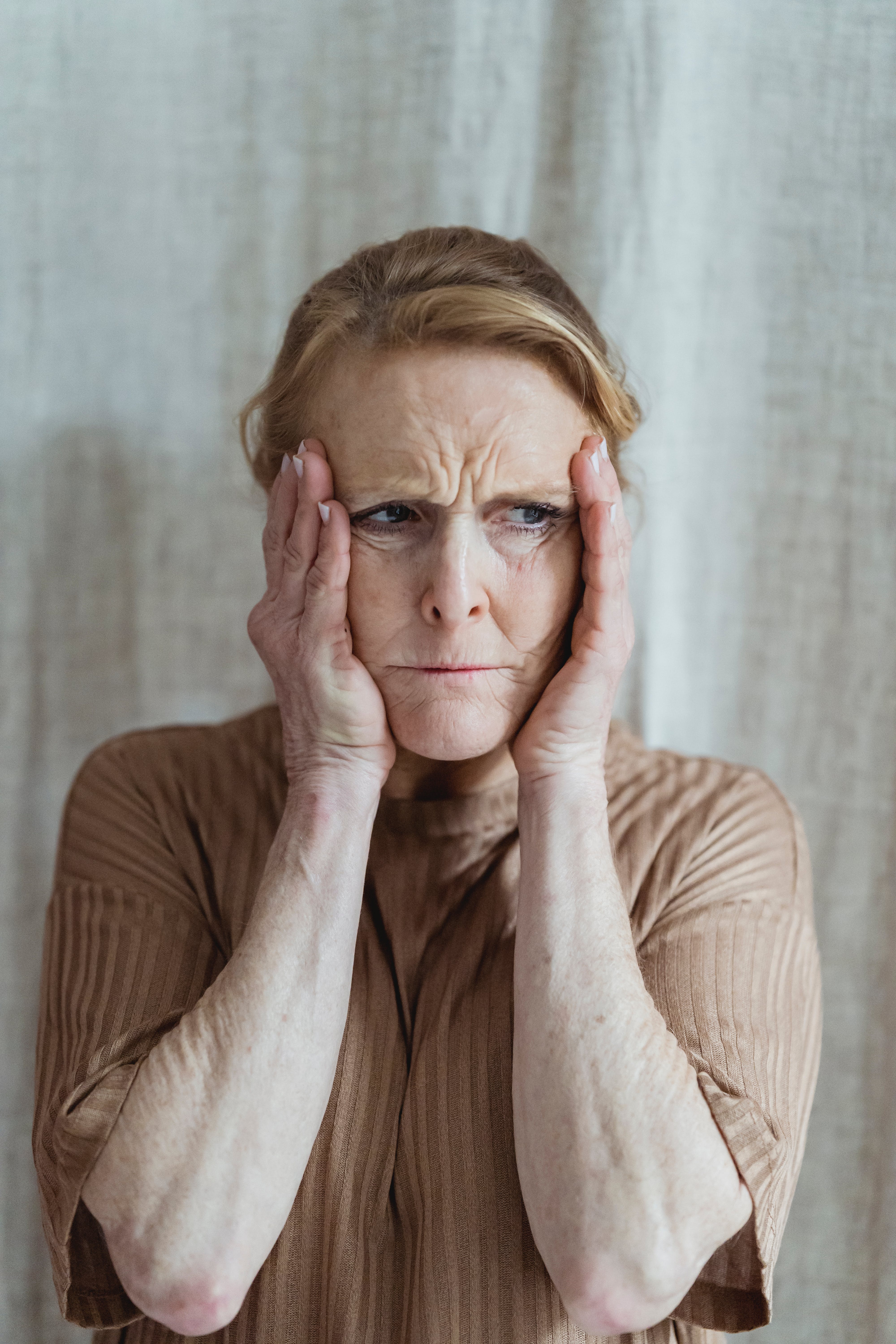 Una mujer mayor angustiada sujetándose la cara con ambas manos | Foto: Pexels