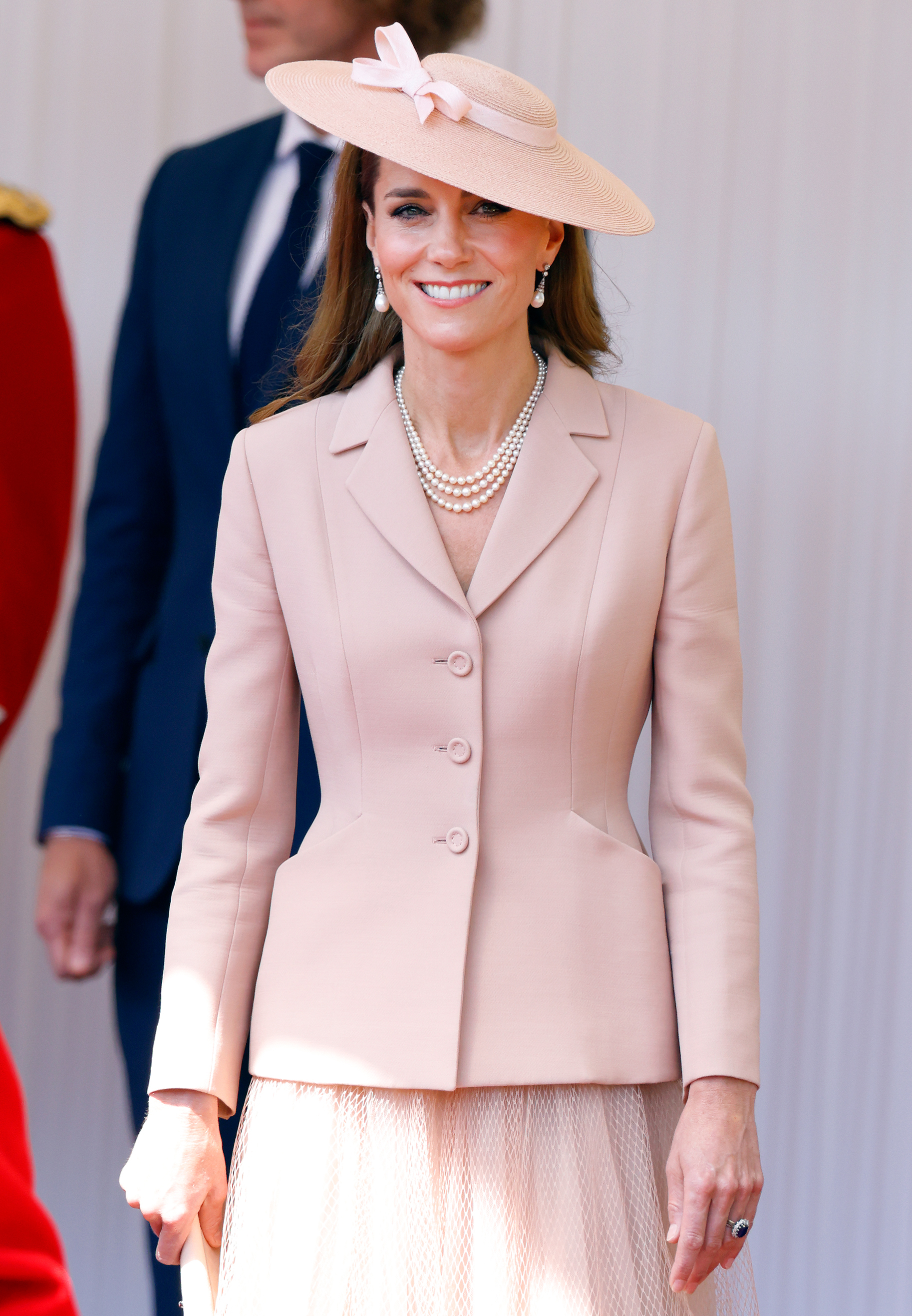 Catherine, princesa de Gales, sonríe en la tribuna real de Datchet Road, Windsor, Inglaterra, durante la bienvenida oficial al presidente francés Emmanuel Macron y Brigitte Macron el 8 de julio de 2025. En un guiño a la alta costura francesa, luce una chaqueta Bar entallada de Christian Dior en rosa pálido, con falda de tul plisada a juego, collar de perlas de tres vueltas de la reina Elizabeth II, pendientes de perlas y sombrero inclinado de ala ancha con un delicado lazo. | Fuente: Getty Images