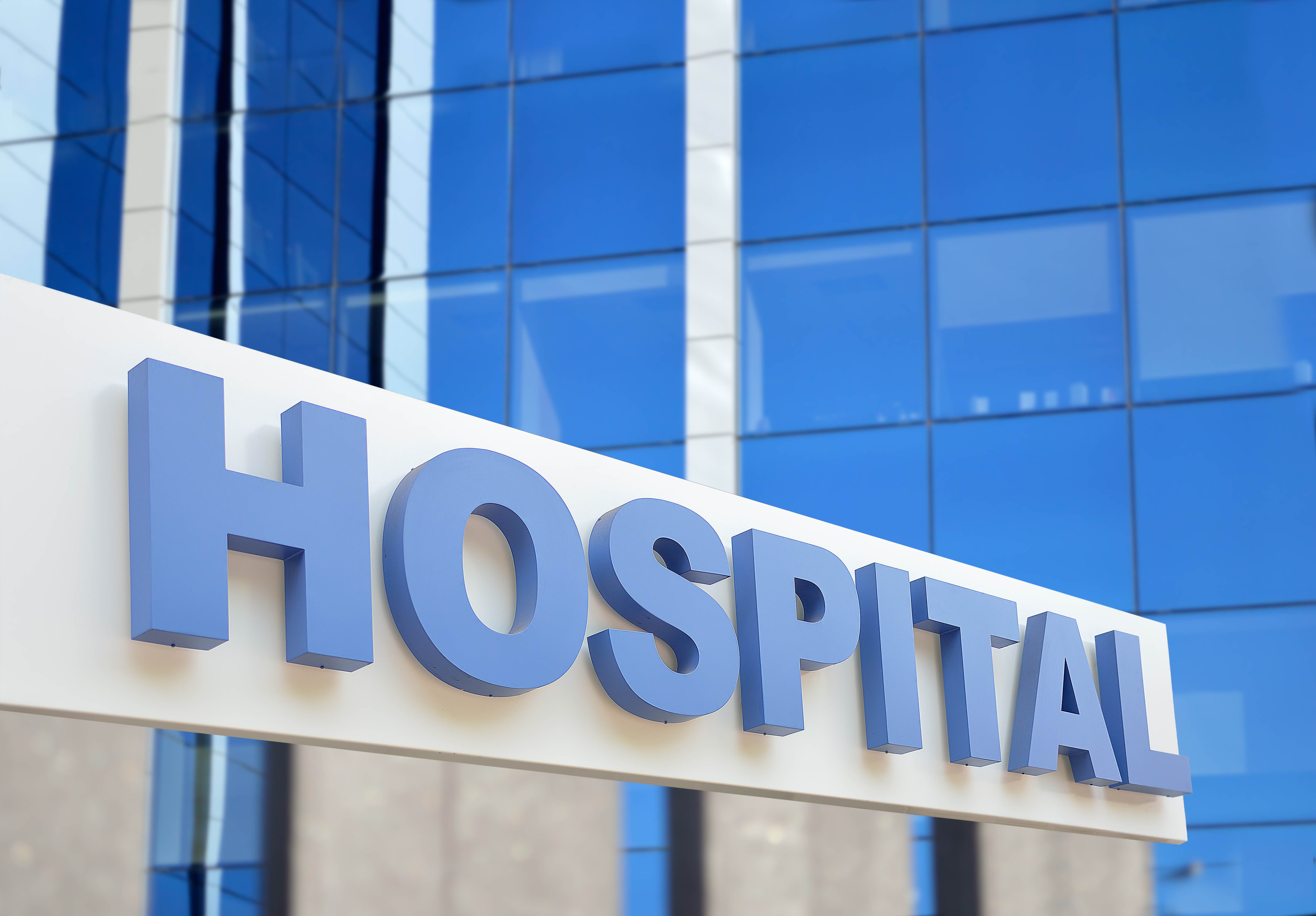 Primer plano del letrero del edificio del hospital, con el cielo reflejándose en el cristal. | Fuente: Shutterstock